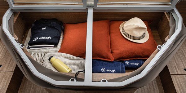 View inside an RV rental's clever storage compartment, neatly filled with clothes, pillows, a hat, bottle, and towels.. Elnagh BARON 579 2024