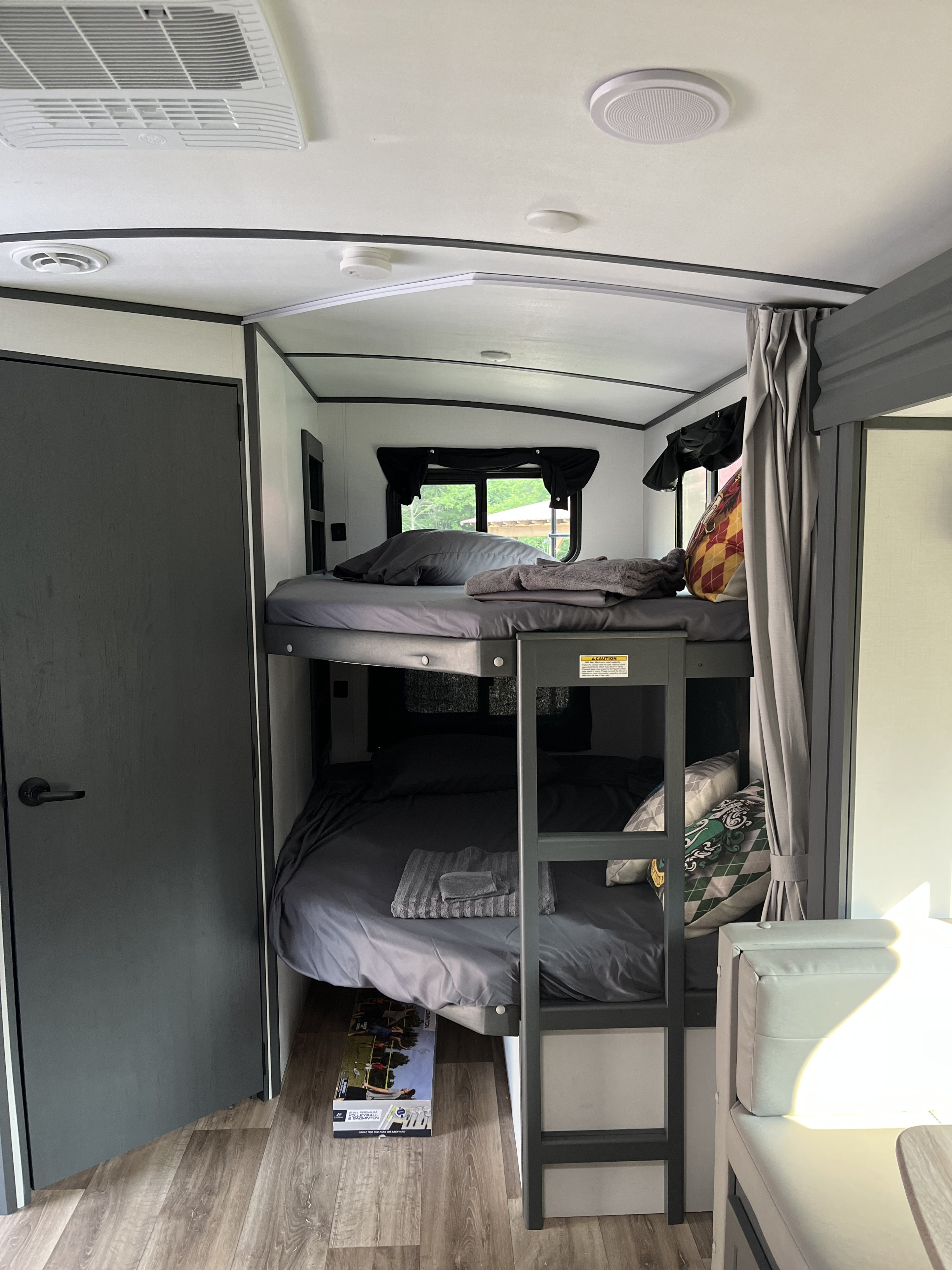 Modern **RV rental** bunk beds. Gray bedding, ladder, ceiling AC, and a dark door complete this compact sleeping space.. Keystone RV Bullet Ultra Lite 2022