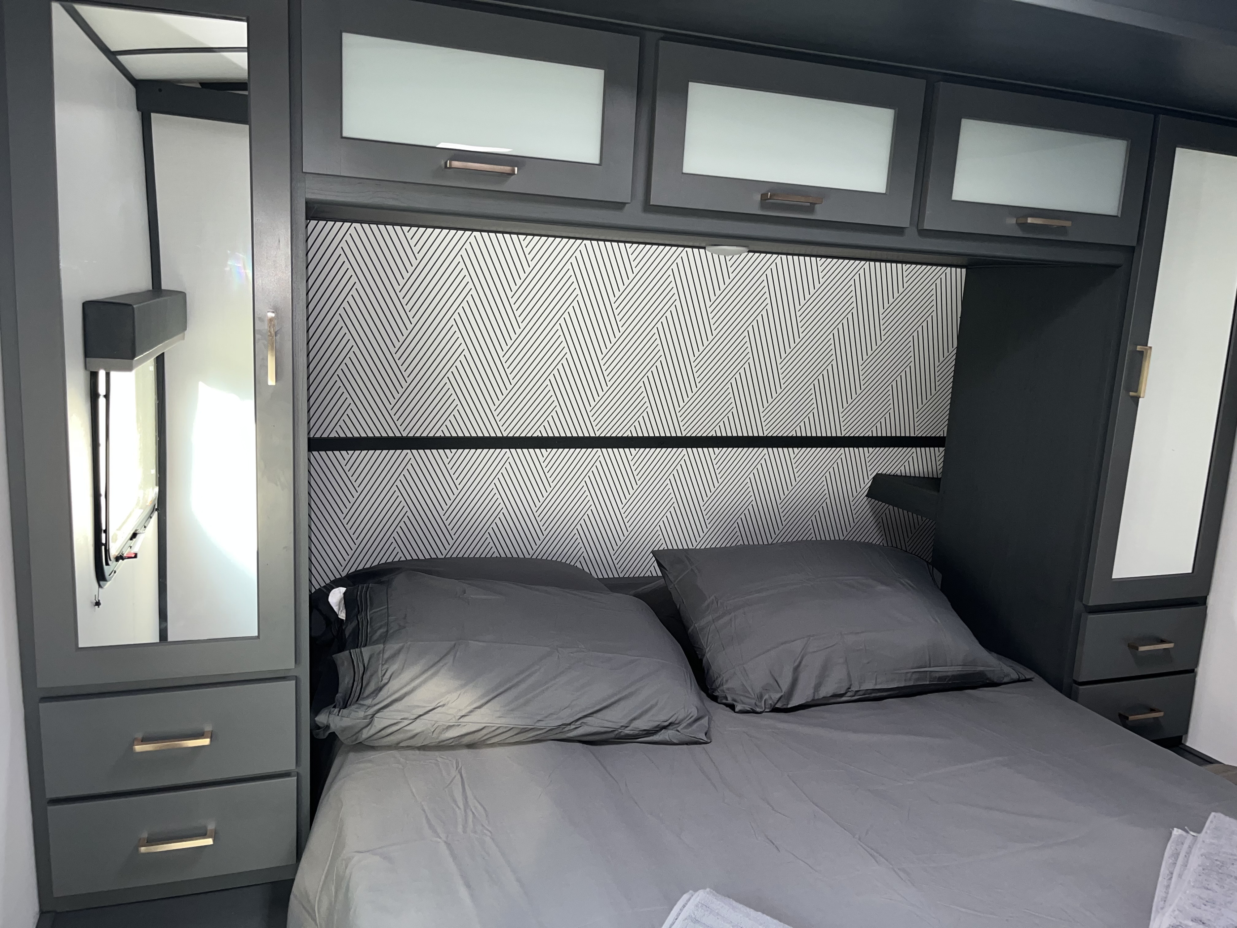 Modern RV rental bedroom featuring gray bedding, a patterned headboard, and ample built-in storage with mirrored cabinets.. Keystone RV Bullet Ultra Lite 2022