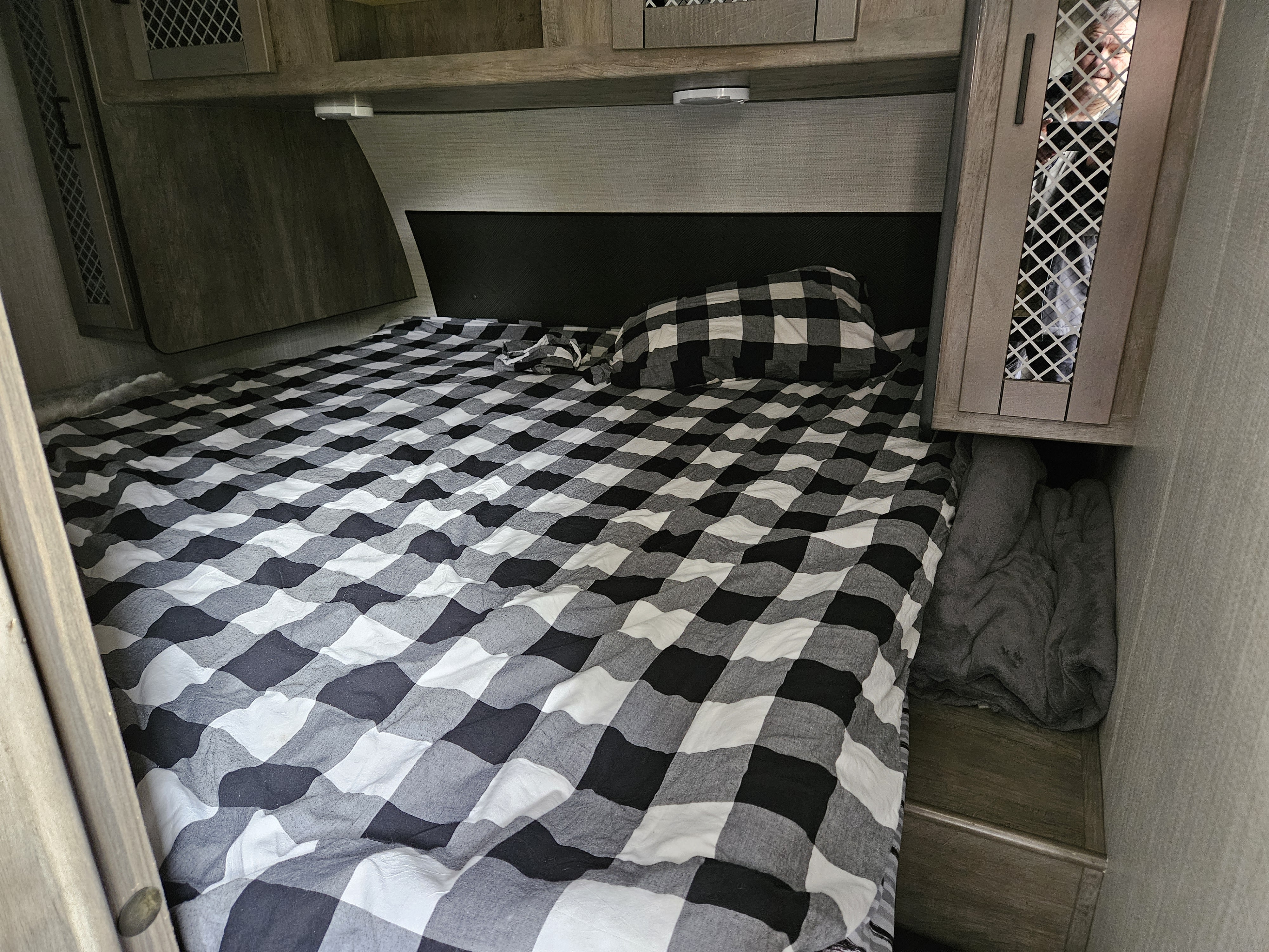 This RV rental bedroom features a comfy bed with black and white plaid bedding, surrounded by wood-toned cabinets.. Heartland RVs North Trail 2021