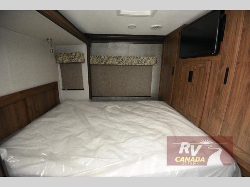 This RV rental features a cozy bedroom with a spacious bed, wooden headboard, built-in TV, and cabinets for storage.. Forest River 3011DSF 2019