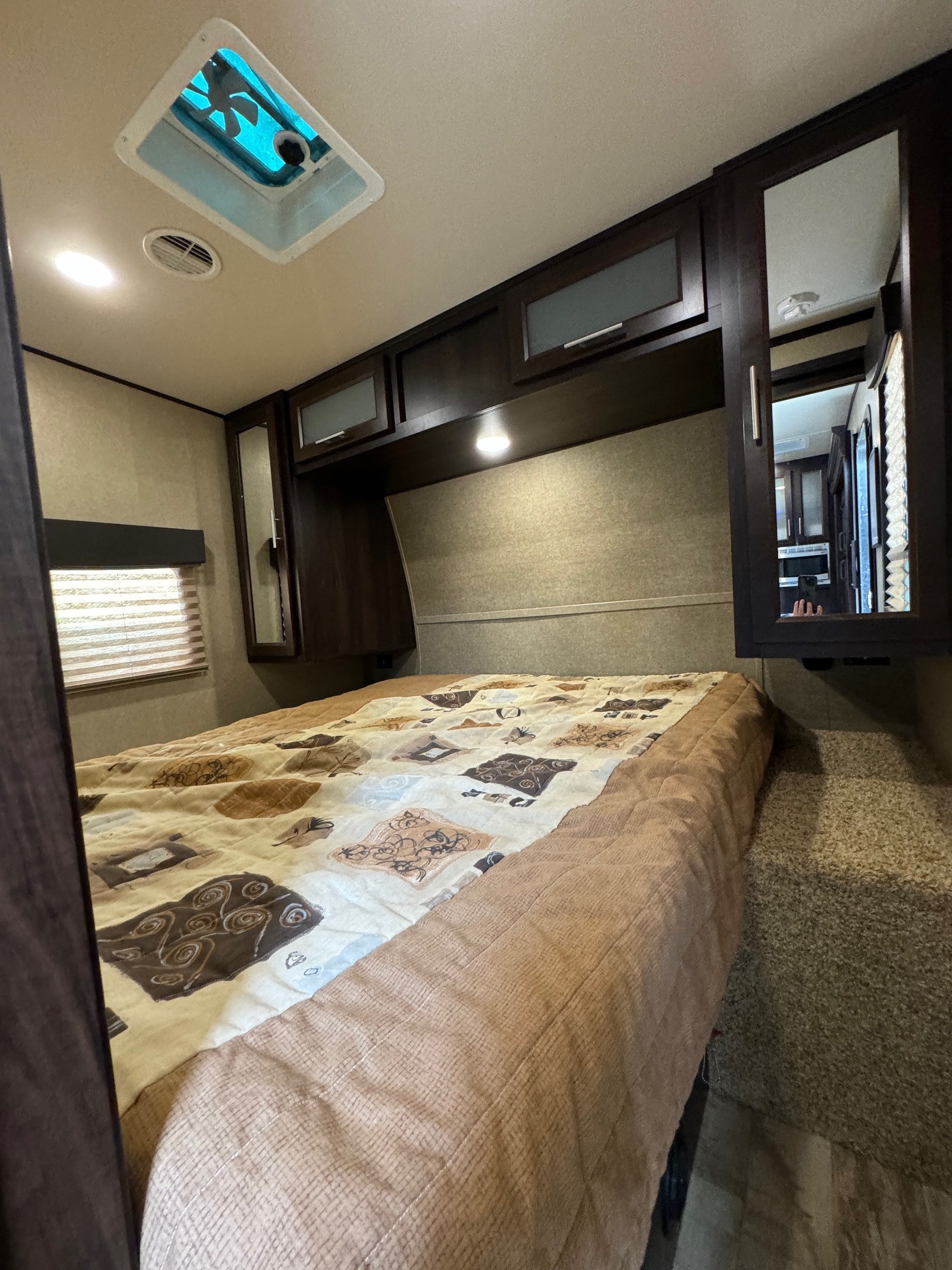 RV rental bedroom showcasing a cozy bed with patterned comforter, dark cabinetry, and an overhead vent.. Forest River XLR HyperLite Toy Hauler 2017