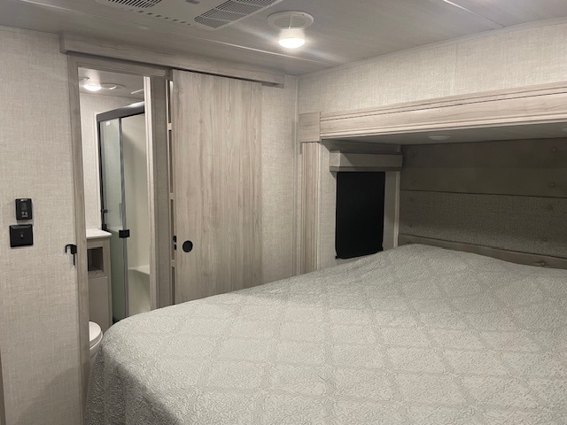 Spacious RV rental bedroom featuring a comfy bed and sliding door access to a private bathroom with a shower and toilet.. Tandara East To West 2022