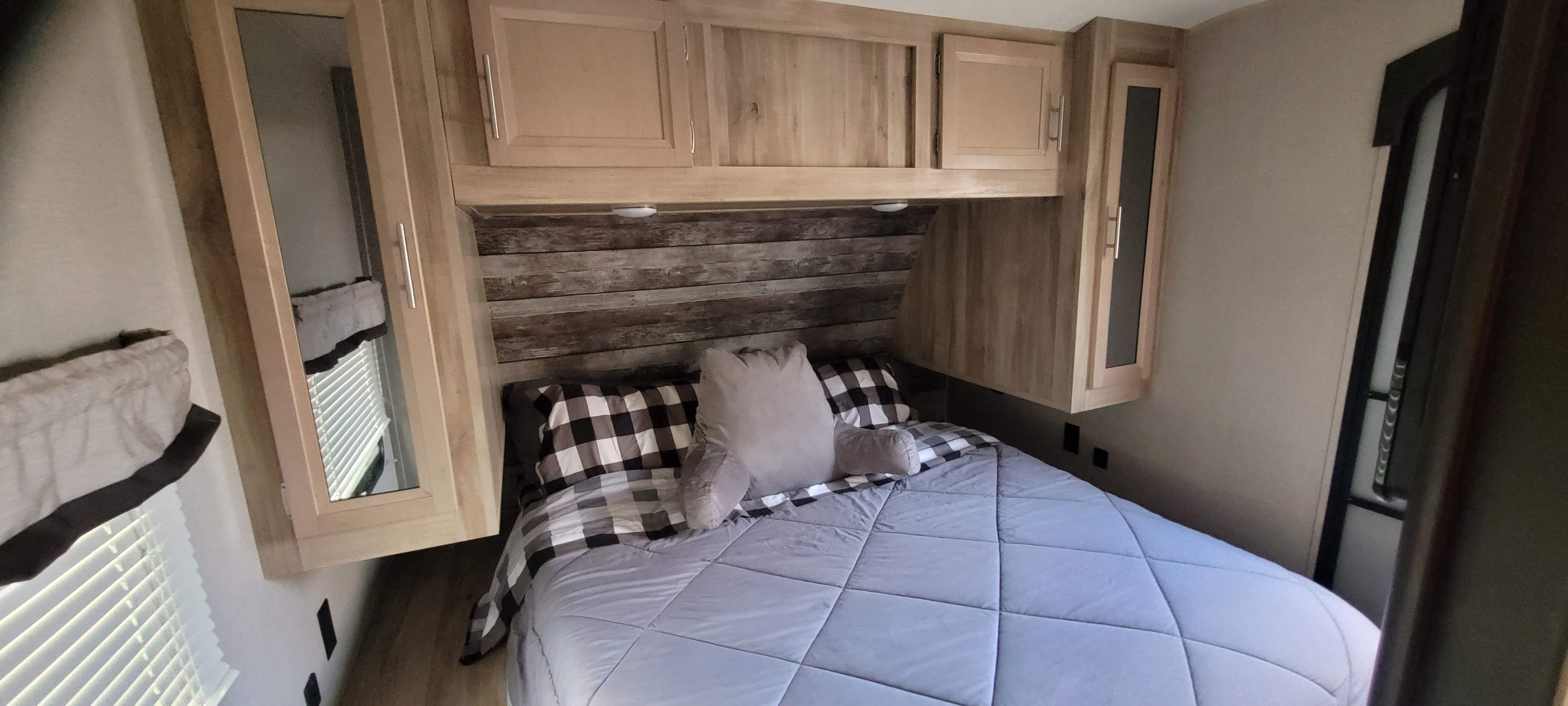 Cozy RV rental bedroom featuring a bed with buffalo check bedding, light wood cabinets, and rustic wood accent wall.. Coachmen Other 2021