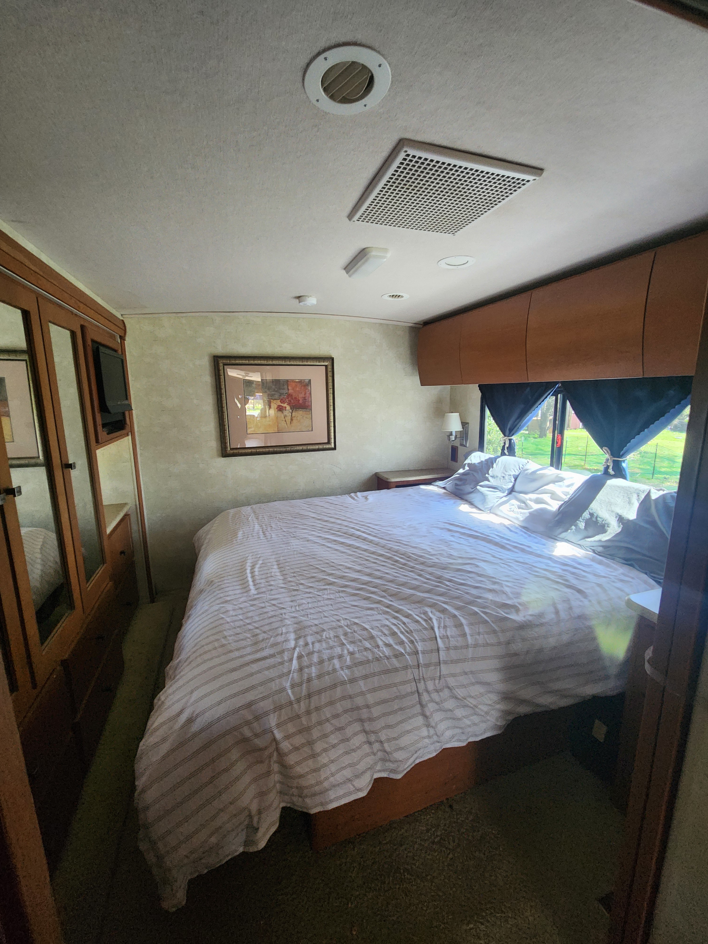 Interior of an RV rental bedroom featuring a large bed with striped covers, a wall-mounted TV, and overhead storage.. Itasca Sunova 2008