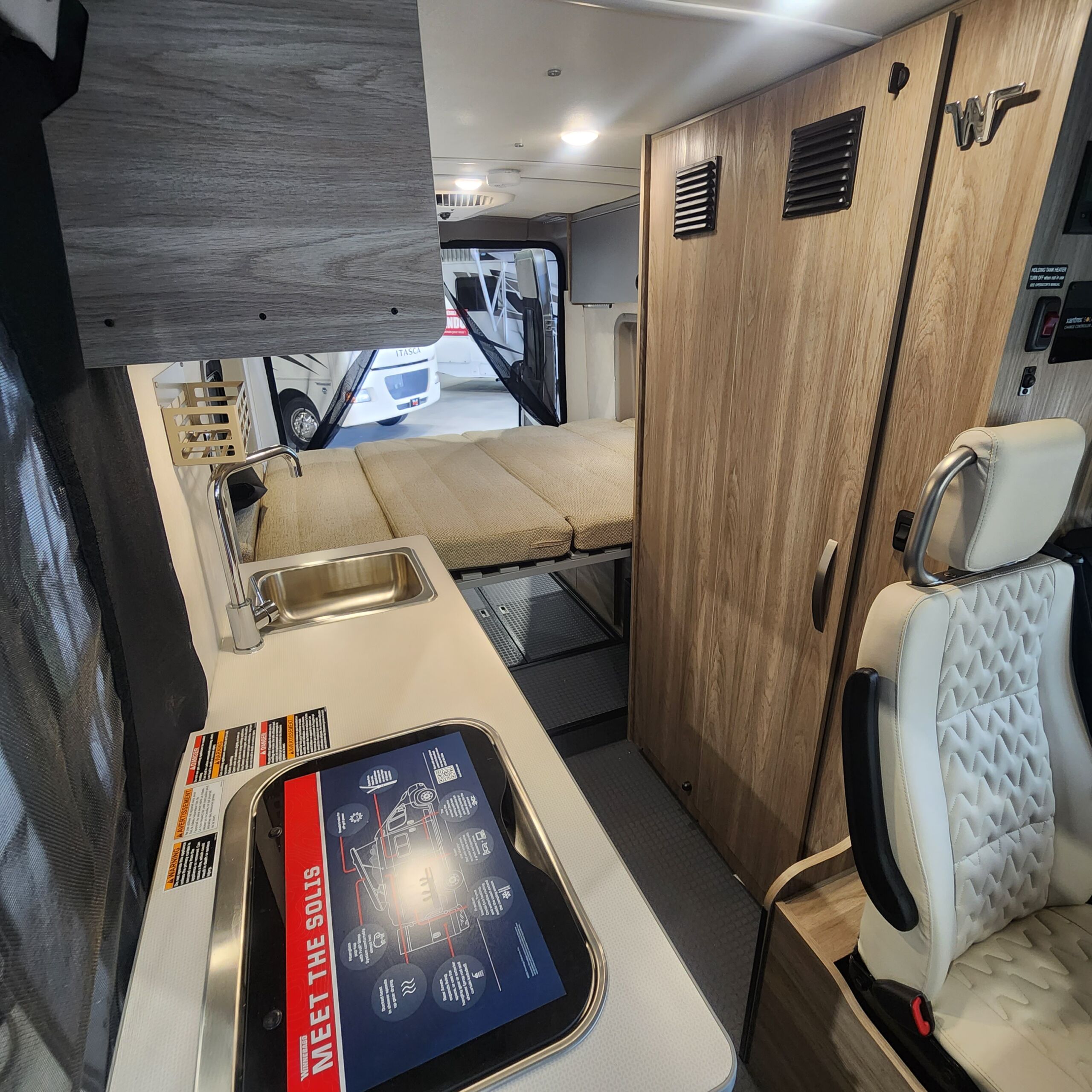 Inside a Winnebago Solis rv rental: a light-toned interior with a kitchen sink, convertible bed, and passenger seat.. Winnebago Solis 2023