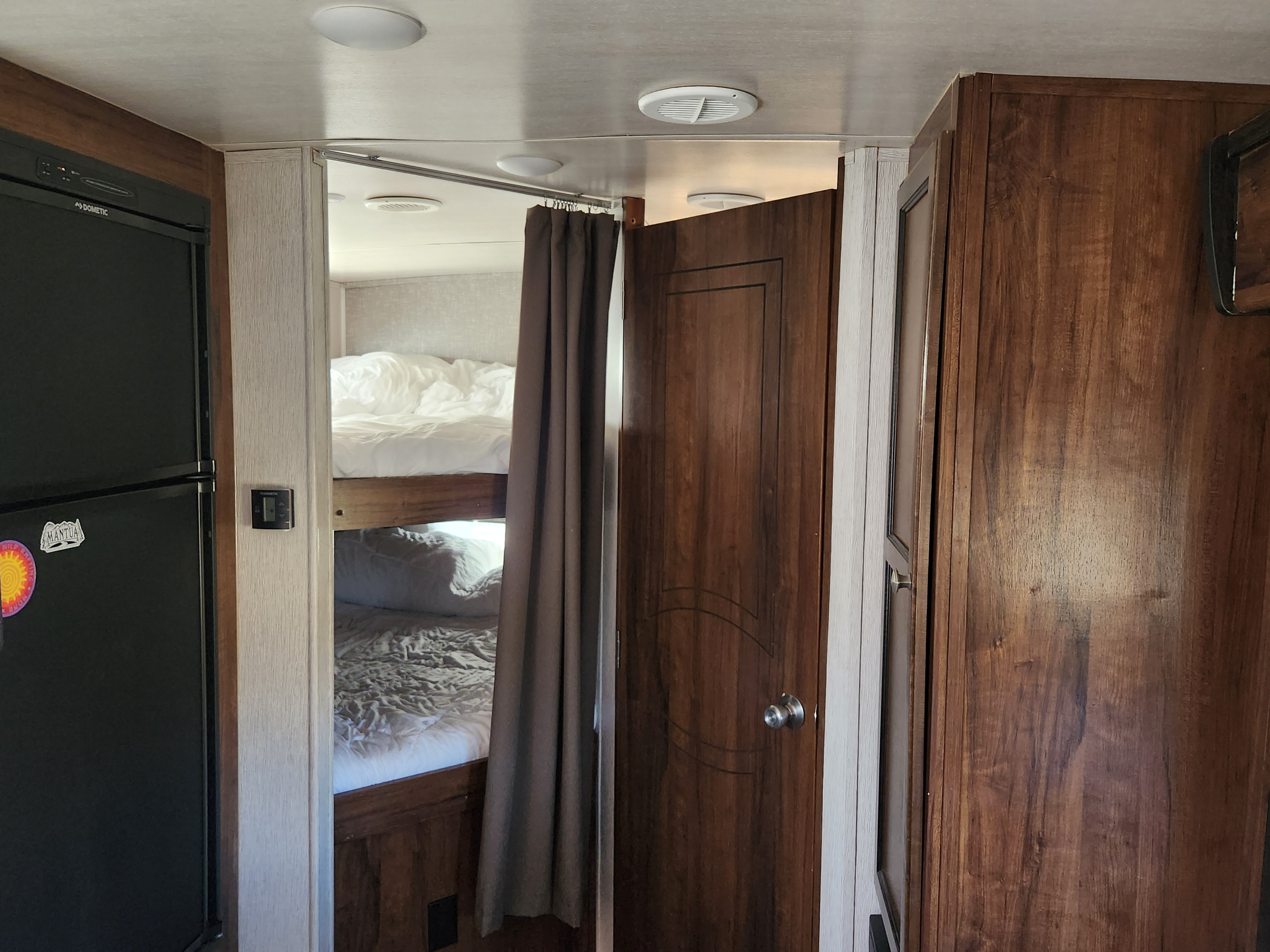 Inside an RV rental: a compact living space featuring a Dometic fridge, bunk beds with white linens, and a private wood door.. Heartland Wilderness 2019