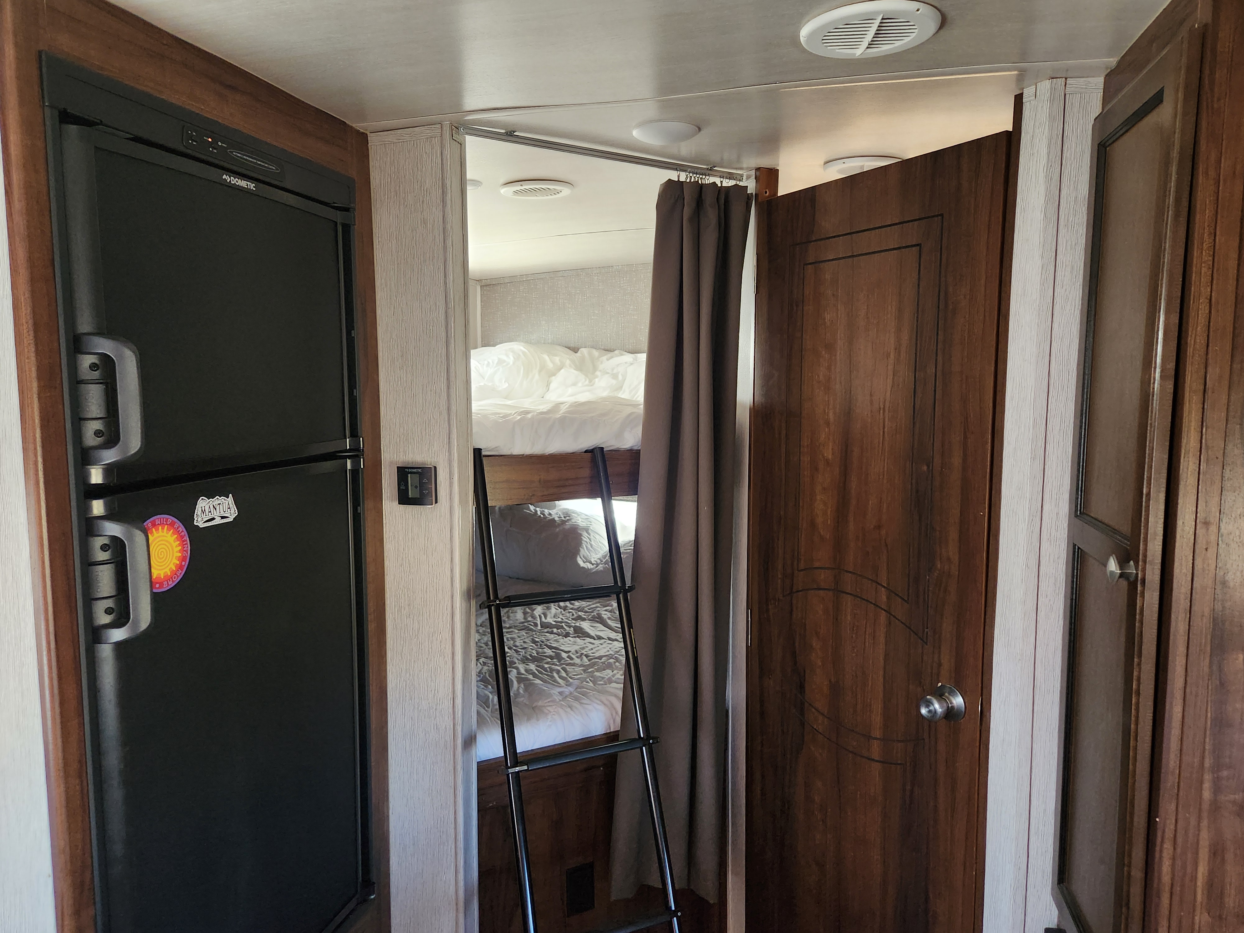 RV rental interior: Dometic refrigerator, control panel, and a cozy bunk bed area with ladder and curtain.. Heartland Wilderness 2019
