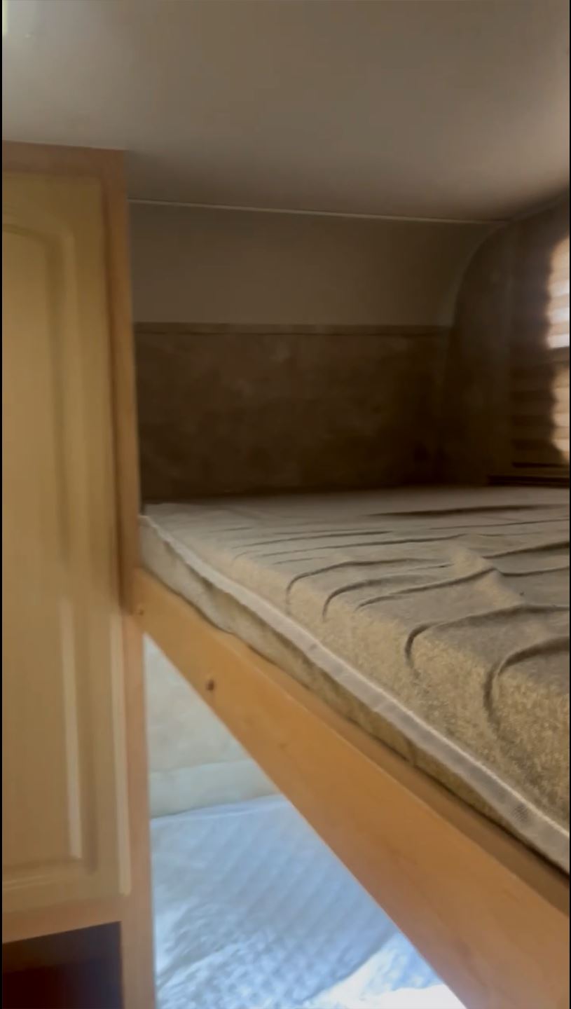 RV rental's cozy bunk bed features a textured mattress and wood frame, with another sleeping area below.. Coachmen Captiva 2007