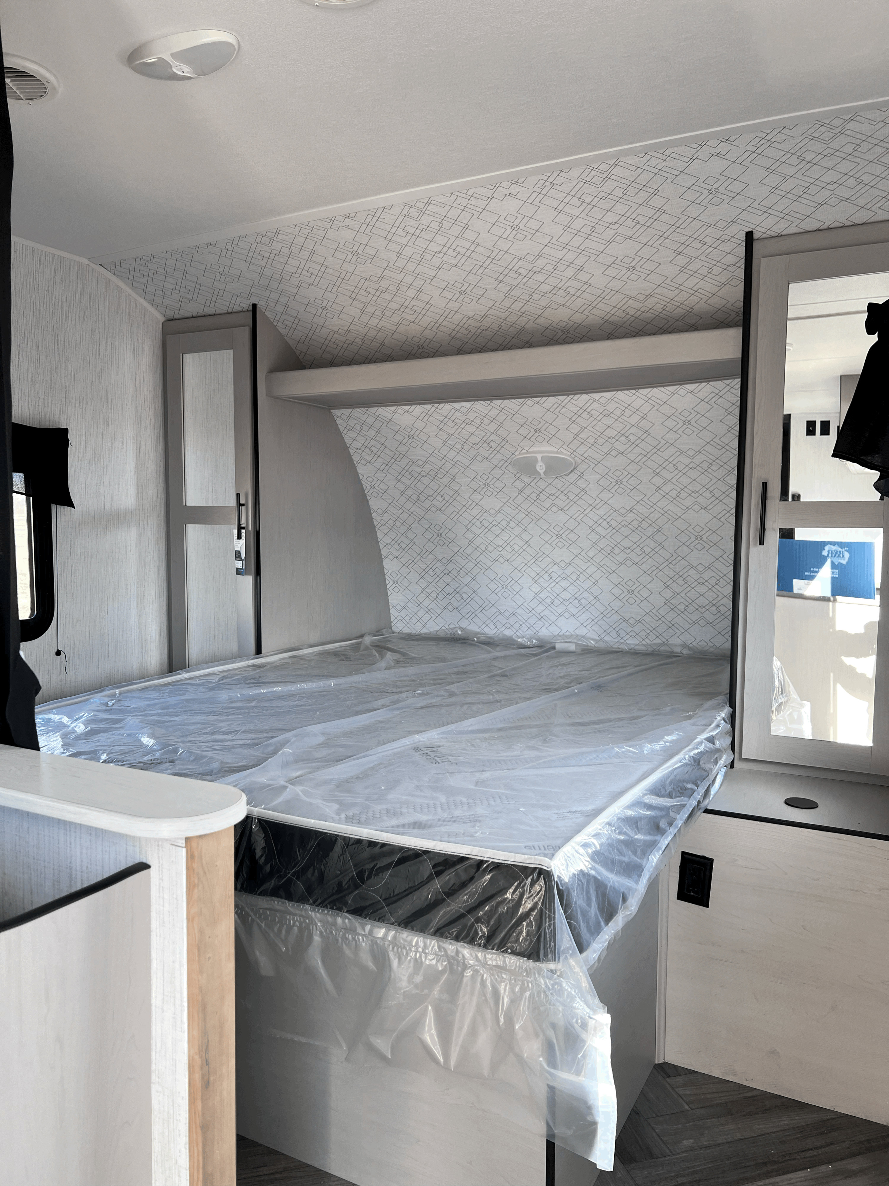 Inside a modern RV rental, featuring a spacious bedroom with a new, plastic-wrapped mattress and sleek interior design.. Heartland RVs Prowler 2023