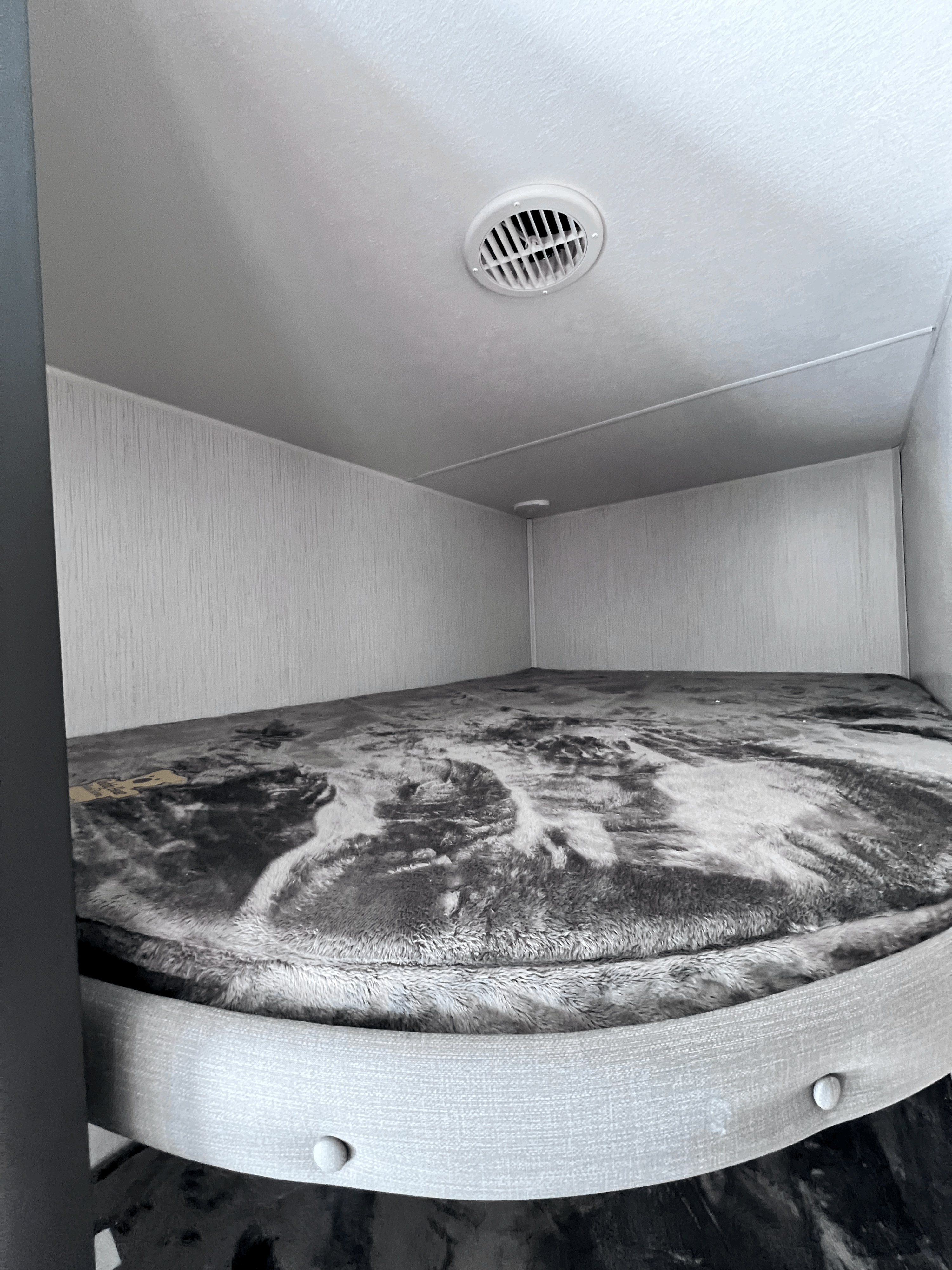 Cozy RV rental bunk bed with a fluffy blanket and ceiling vent. A compact and comfortable sleeping area.. Heartland RVs Prowler 2023