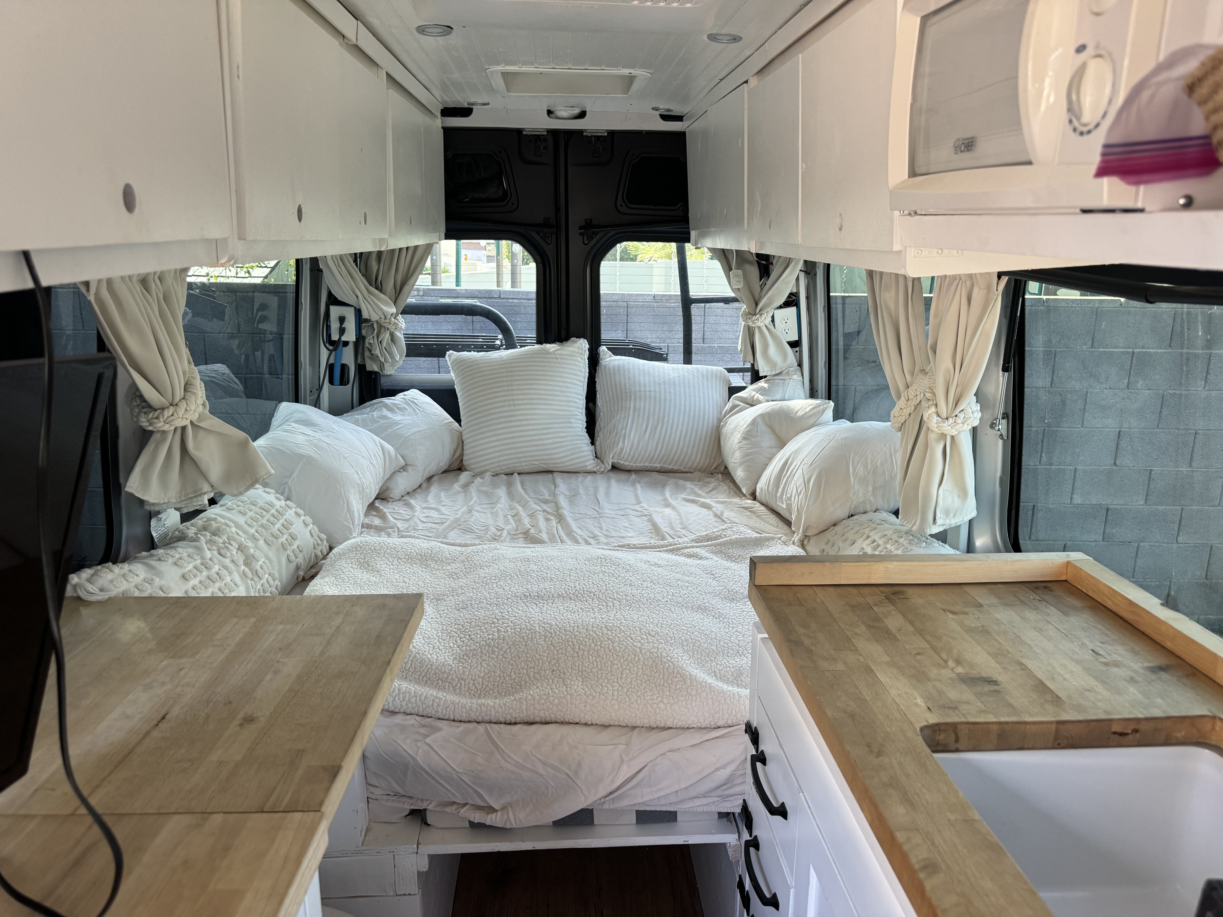 View from front of an RV rental showing bed with white linens, overhead cabinets, & wood counters with sink.. wdzpe8cd0jp648573 2500 2018