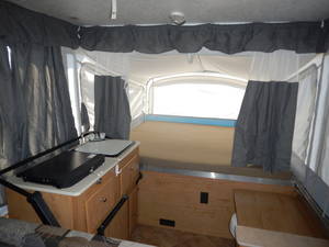RV rental: Step inside this pop-up camper. Features a compact kitchen with sink, bed area with bright window, and gray curtains.. Coleman Santa fe 2010
