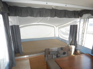 Interior of a pop-up RV rental: spacious bed area with white canvas walls and dark curtains, ideal for camping adventures.. Coleman Santa fe 2010