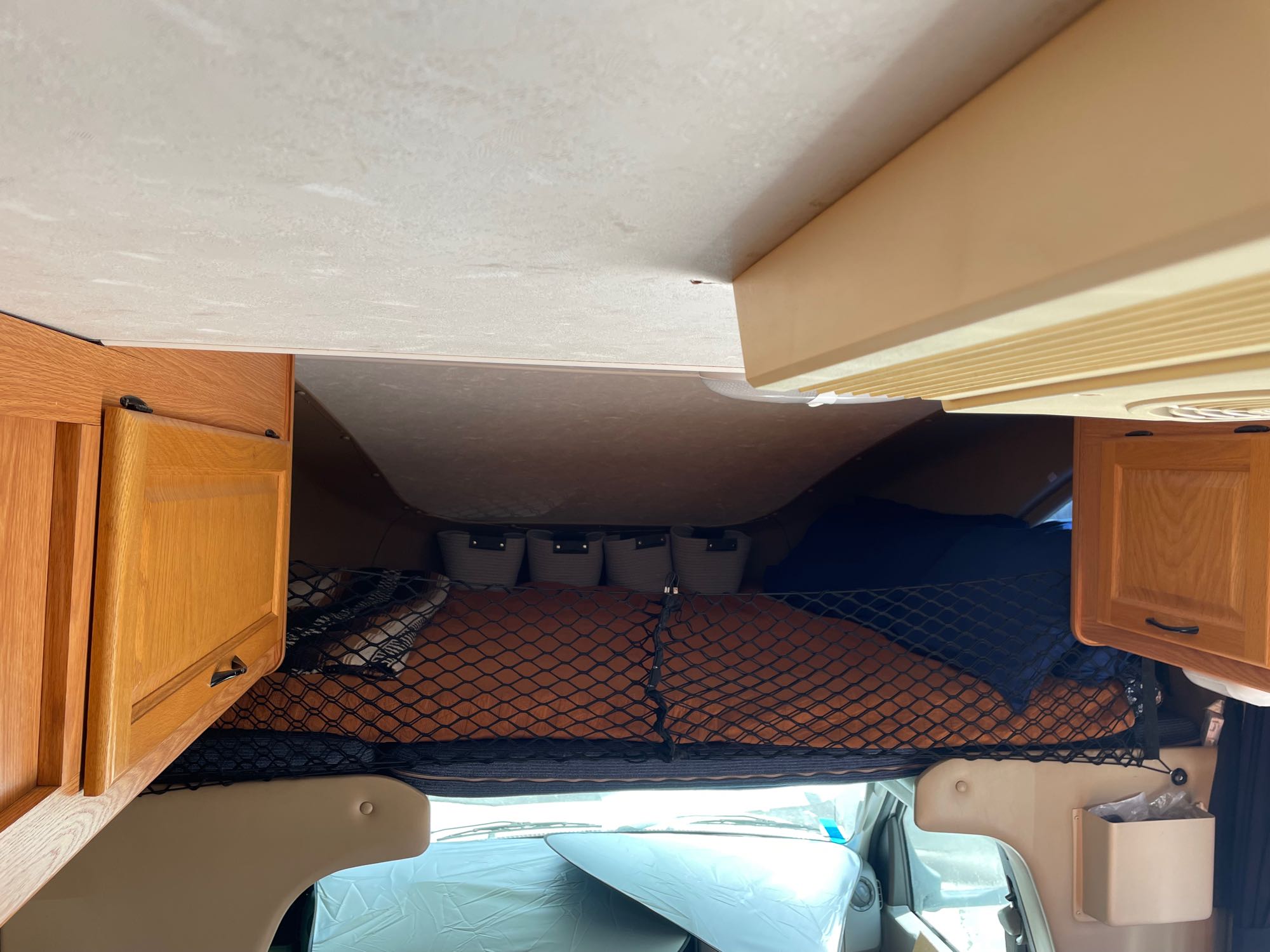 RV rental interior: cab-over bunk with net storage, cozy sleeping area above driver's cabin, and wood cabinetry.. Four Winds Majestic 2010