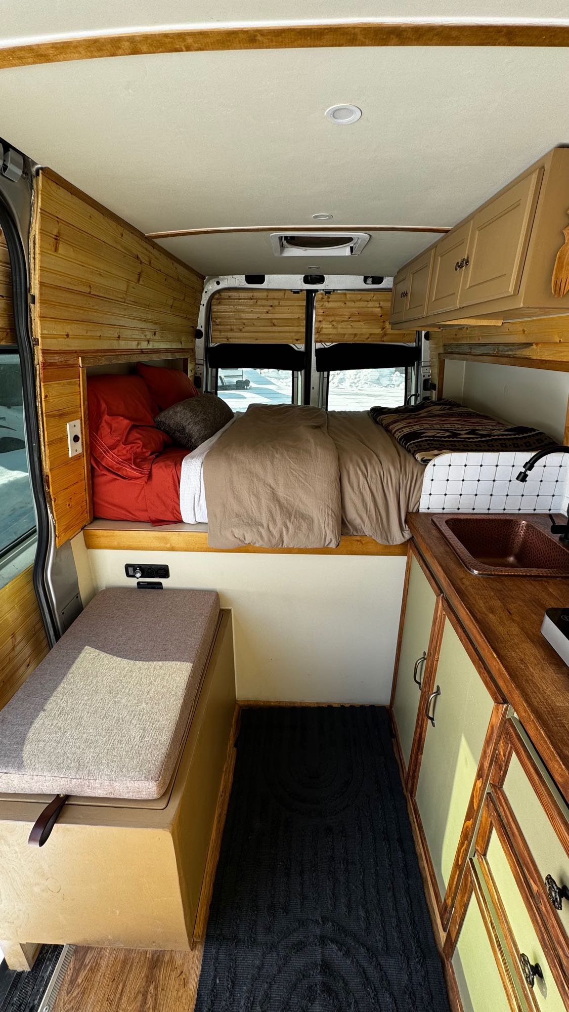 Inside a custom **RV rental**: wood-paneled walls, a comfy bed, kitchen sink, & versatile seating. Ideal for road trips.. Mercedes Sprinter 2019
