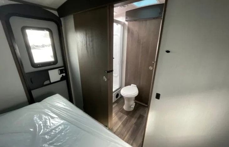 Compact RV rental interior: bedroom with bed, and a private bathroom featuring a toilet and shower stall.. Keystone RV Cougar 2023