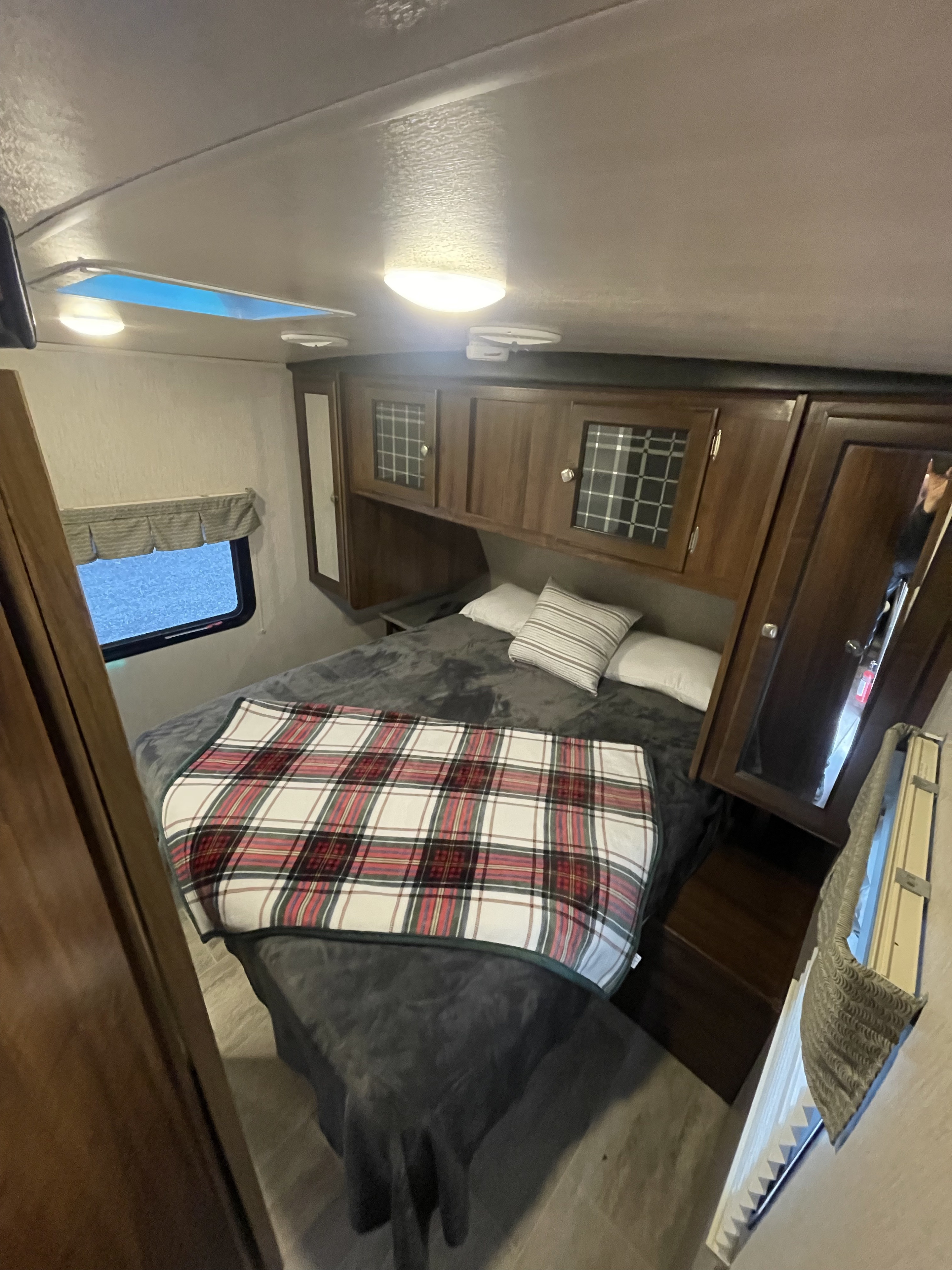 Comfortable RV rental bedroom featuring a plaid blanket, overhead cabinets, window, and skylight for bright stays.. Heartland RVs Mallard 2019
