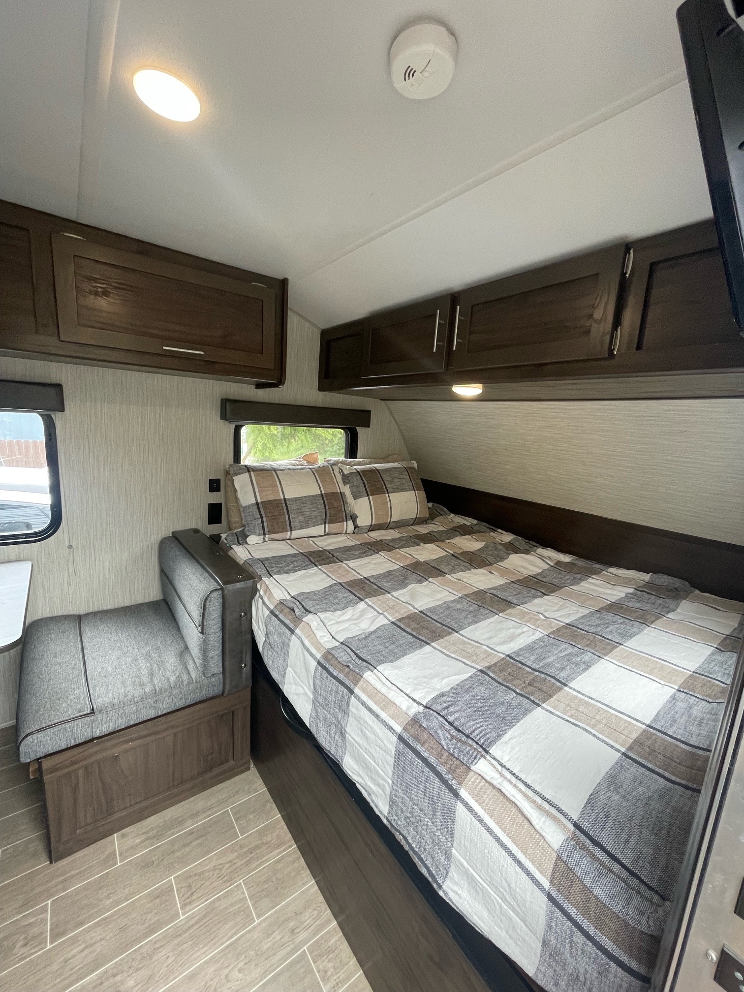 Inside an RV rental: a cozy bedroom with plaid bedding, adjacent seating, and ample storage cabinets.. Forest River Cherokee Wolf Pup 2020