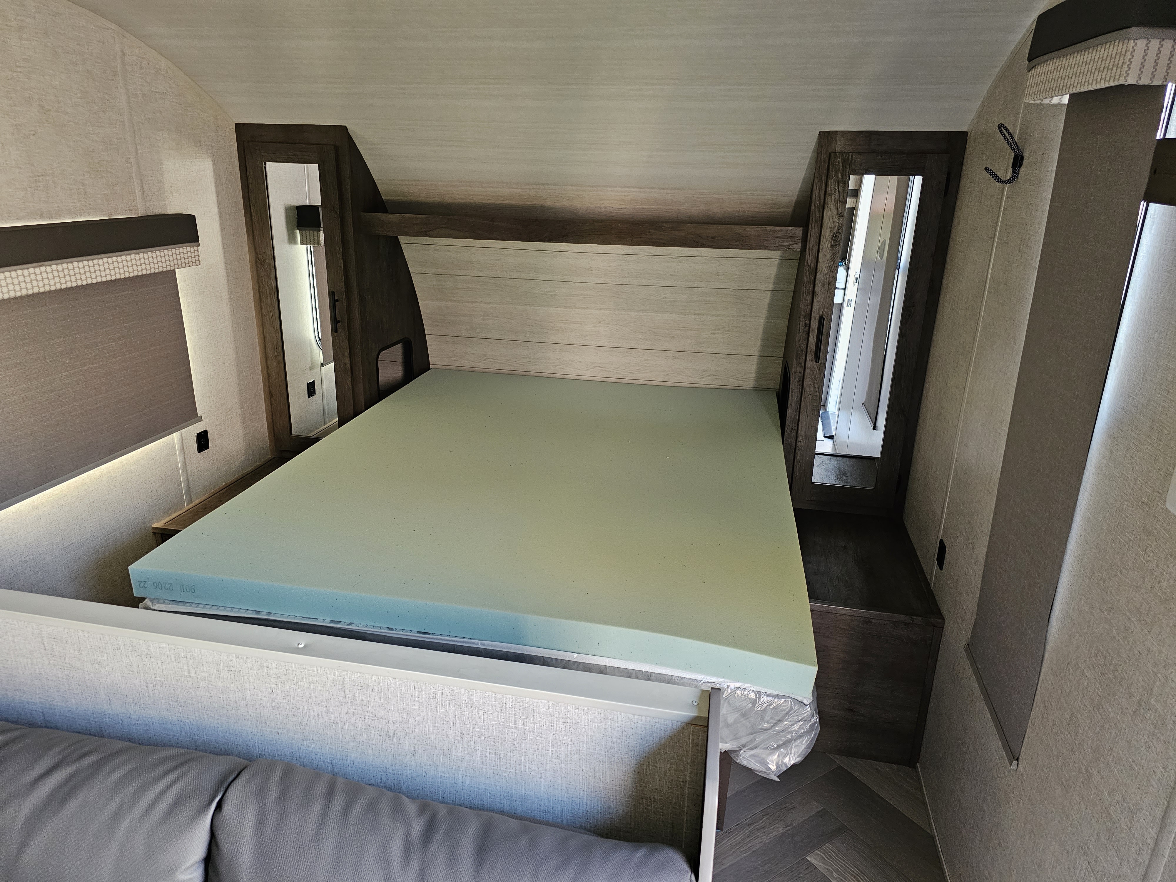 An RV rental's bedroom area, featuring a light green foam mattress, wood headboard, and mirrored closets.. Forest River Wildwood X-Lite 2021