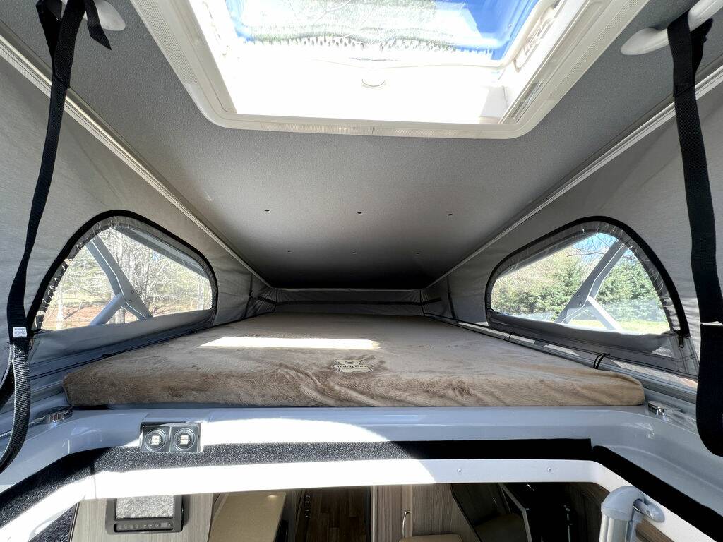 Interior view of a spacious pop-top roof bed in an rv rental camper van. Enjoy elevated sleeping with large side and sky windows.. Thor Sequence 2021
