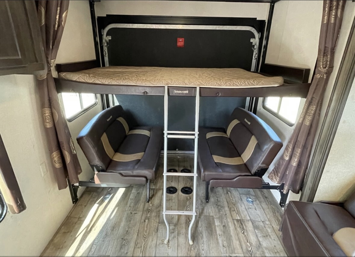 Interior of an RV rental showing a garage area with a drop-down bunk bed, ladder, and two convertible sofa seats.. Forest River Sandstorm 2017