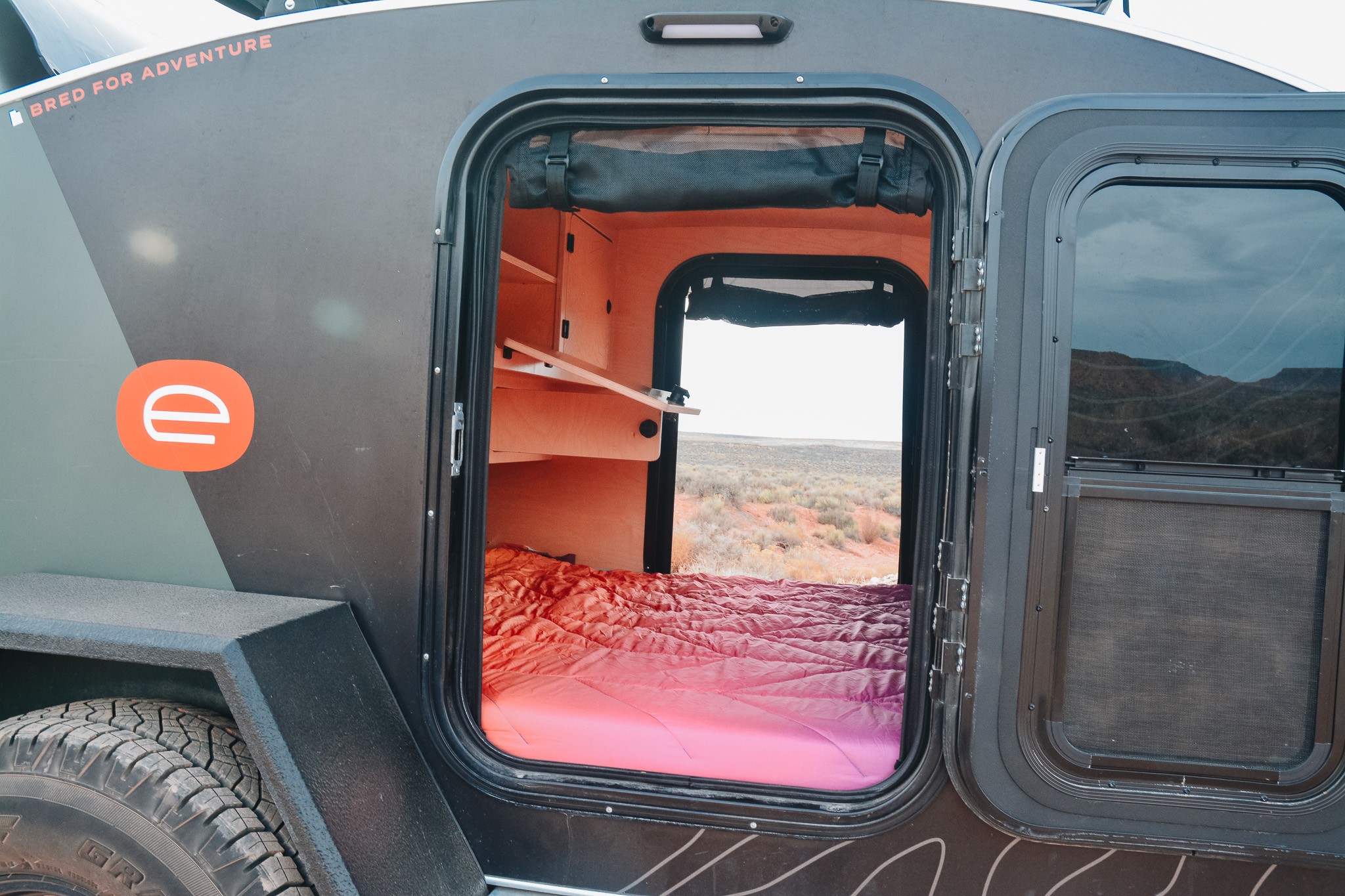 Step inside this compact RV rental! See the cozy bed, built-in shelves, and the desert landscape outside.. Escapod Escapod Trailer 2022