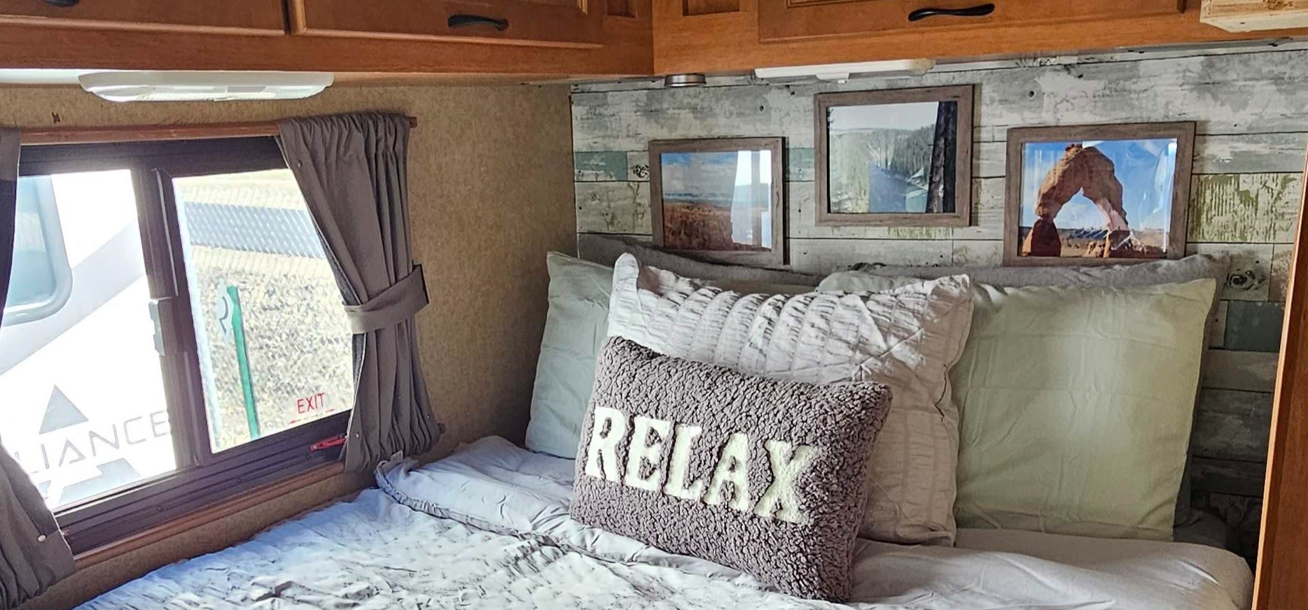 Relaxing RV bedroom with "RELAX" pillow, wood-plank headboard, and window view, perfect for your RV rental getaway.. Thor Majestic 2015