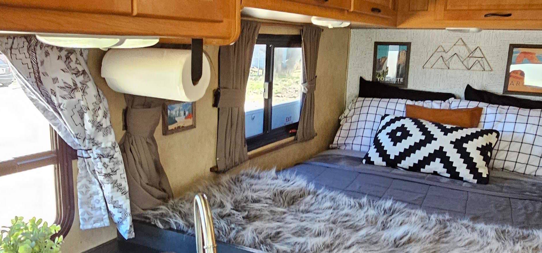 Cozy RV rental interior: a comfy bed with decorative pillows, wall art, windows, and overhead cabinets.. Thor Majestic 2014