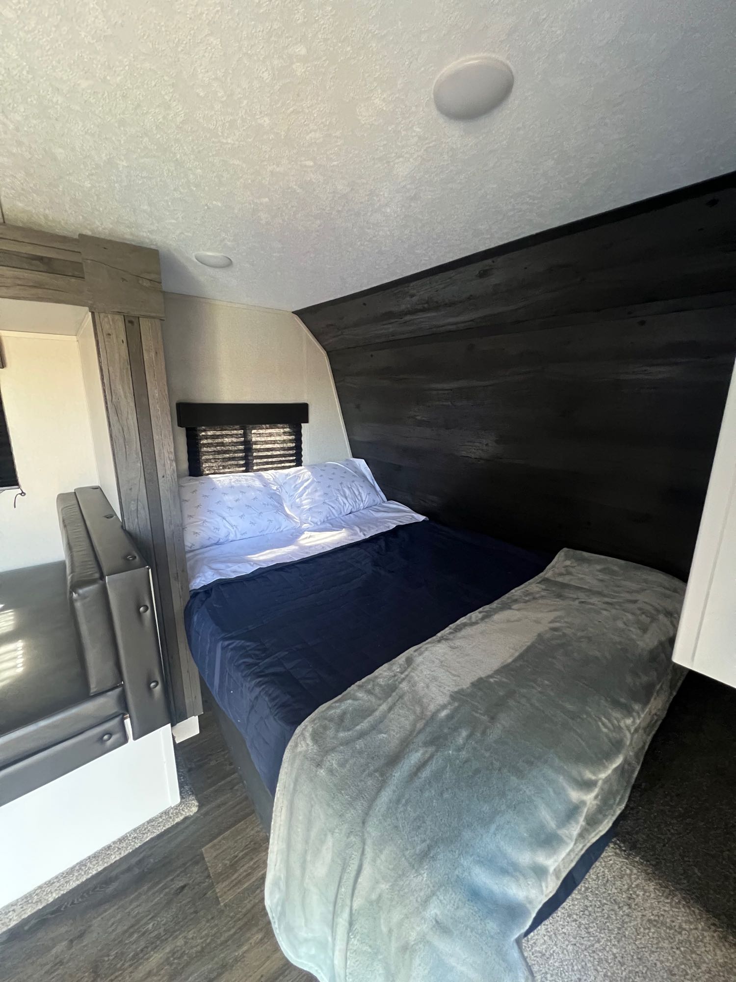 Cozy RV rental bedroom with a comfy bed, blue comforter, dark wood accents, and a versatile dinette on wood-look floor.. Keystone RV Hideout 2021