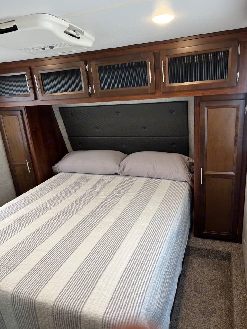 Cozy RV rental bedroom featuring a comfy bed with striped comforter, ample overhead storage, and AC unit.. Forest River Vengeance 2019