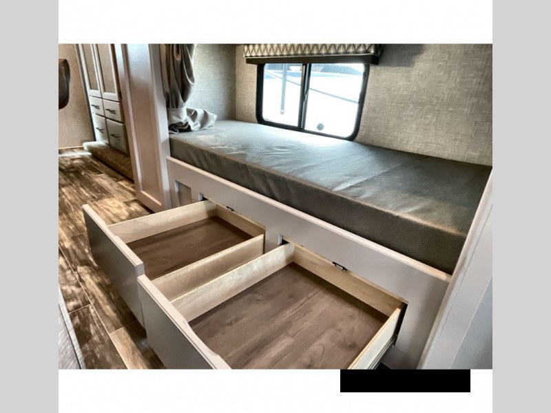 Inside an RV rental: a bunk bed with a gray mattress, a window, and two open pull-out storage drawers below.. Thor Geneva 2023