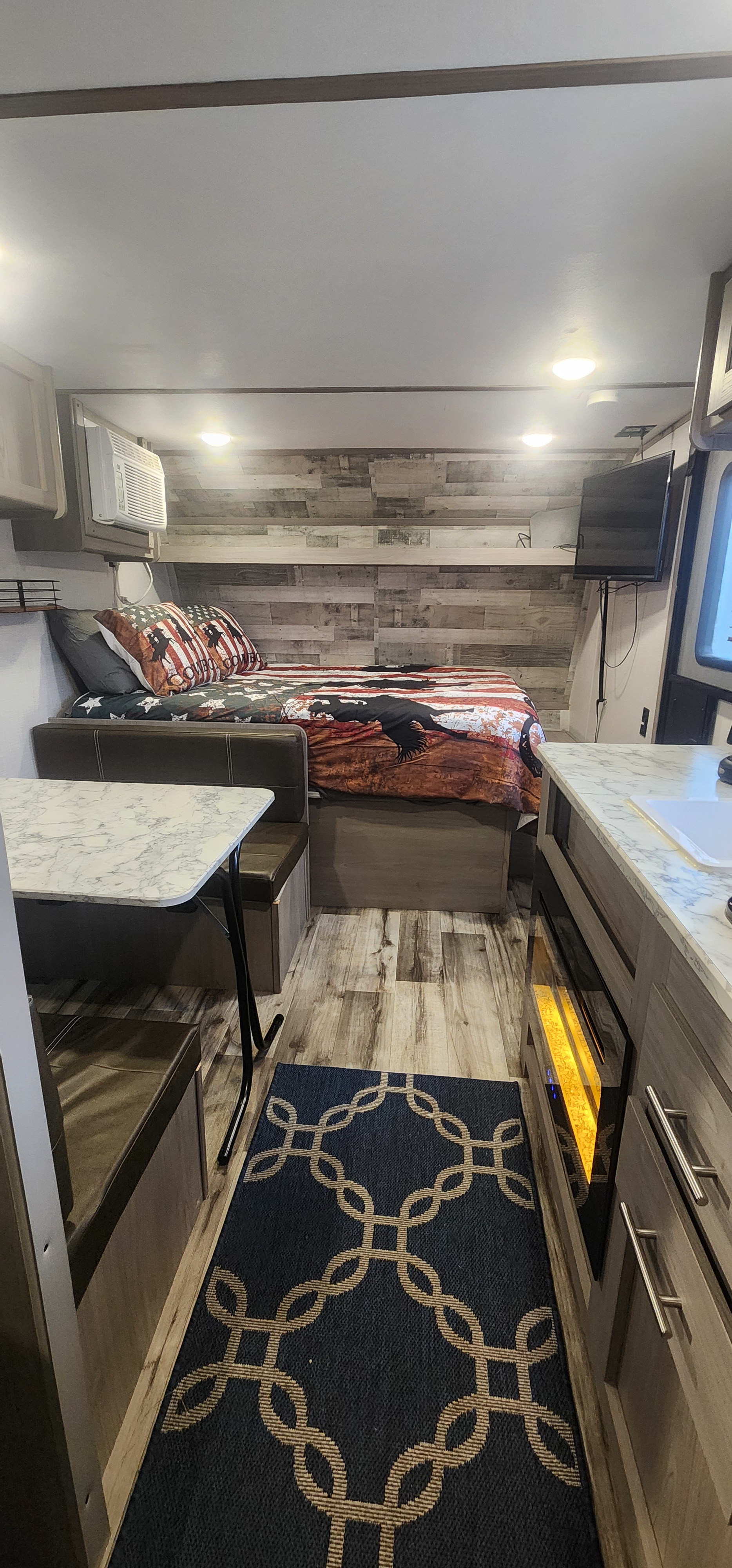 Cozy RV rental interior with a patriotic-themed bed, dining nook, and compact kitchen, complete with a rug.. Dutchmen Coleman Lantern LT 2022