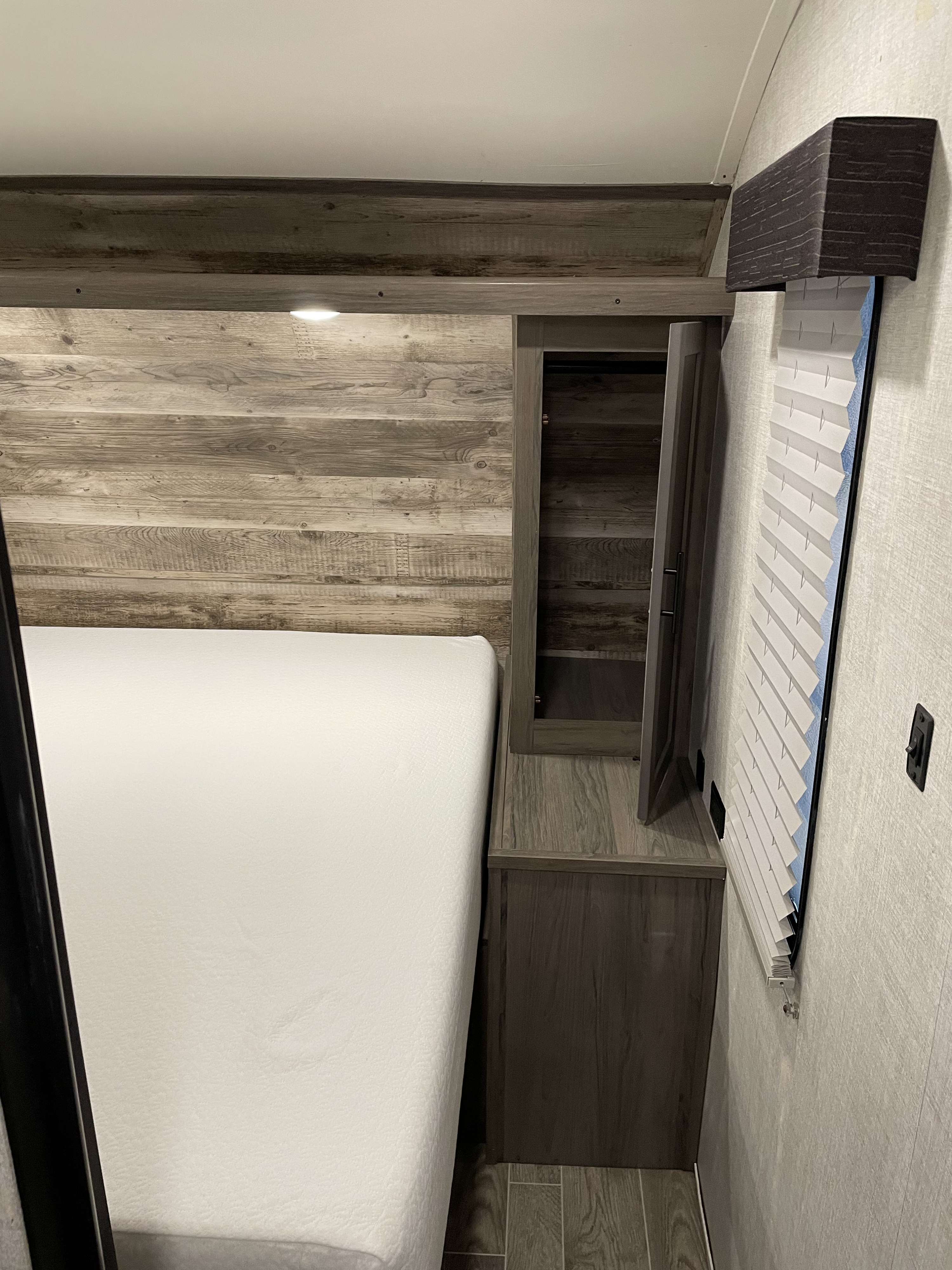 Comfortable RV rental bedroom featuring a white mattress, rustic wood paneling, overhead storage, and window blinds.. Gulf Stream Conquest 2021