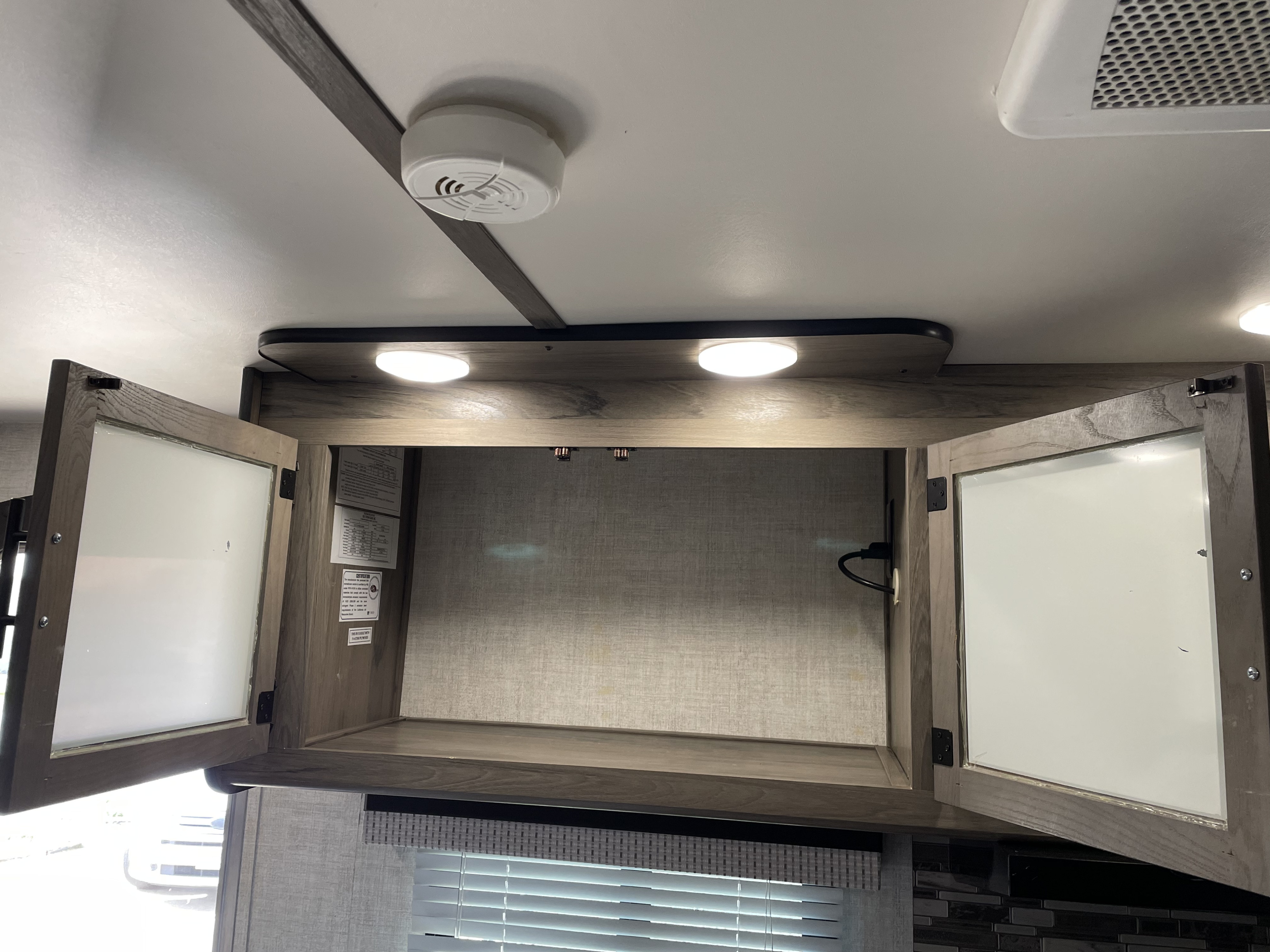 Inside an RV rental: an open overhead cabinet with interior lights, a smoke detector, and ceiling AC vent.. Gulf Stream Conquest 2021