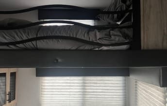 Inside this RV rental: comfy bunk beds with grey bedding. Below, a window with horizontal blinds. Perfect for family travel.. Forest River Cherokee Arctic Wolf 2022
