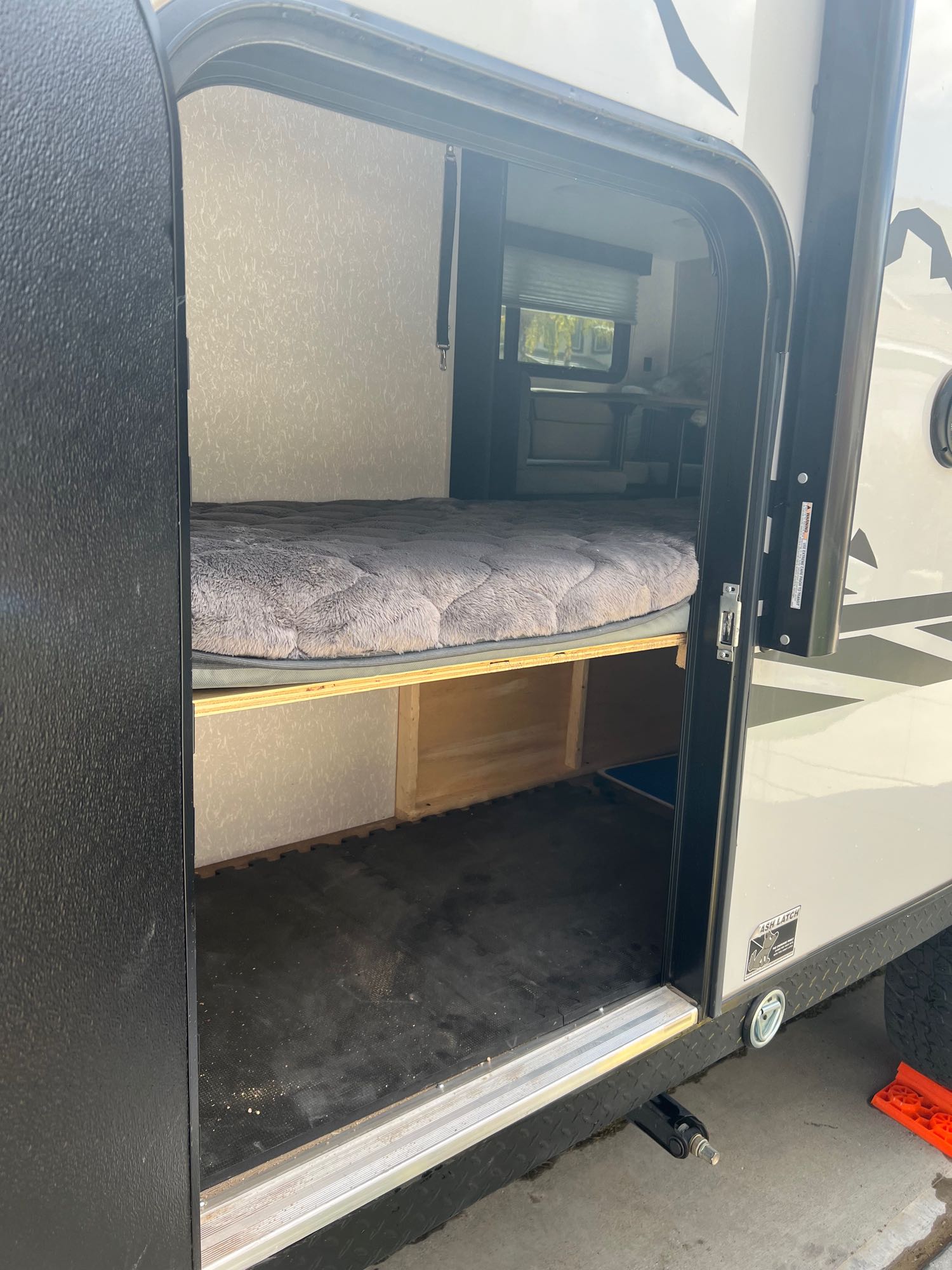 RV rental interior: A cozy, raised bed with storage below, accessible through the open side door of this camper.. Forest River Cherokee Wolf Pup Black Label 2022