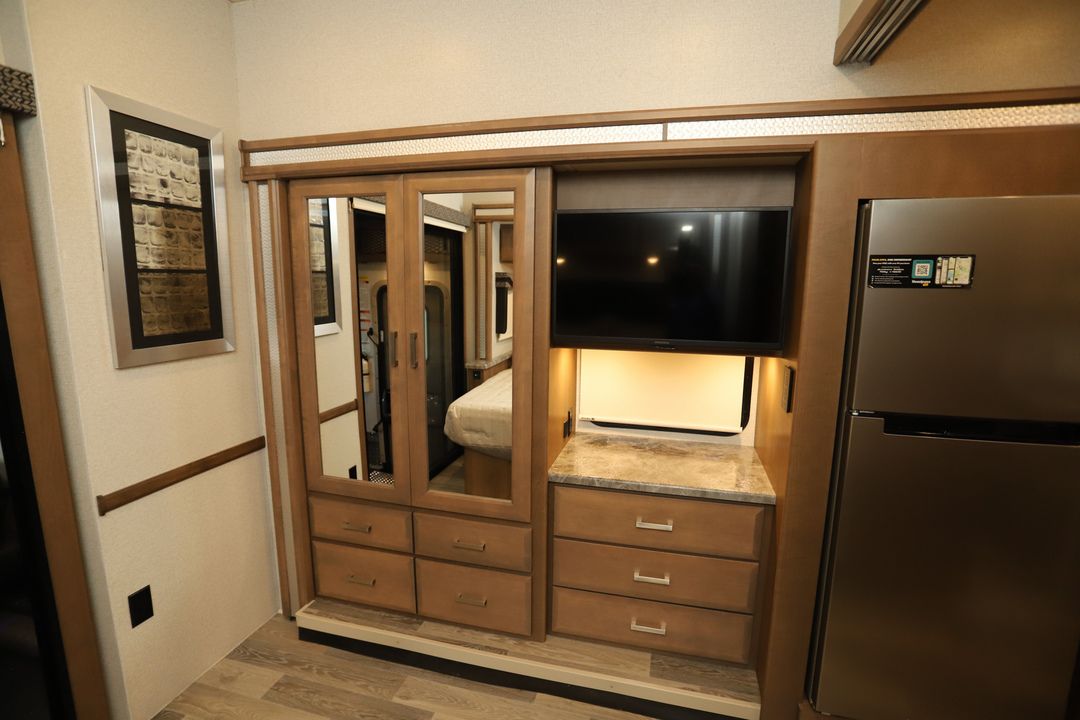RV rental interior with mirrored wardrobe, flat-screen TV, ample storage drawers, and a stainless steel fridge.. Thor Outlaw 2023