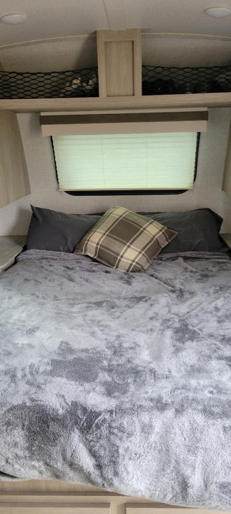 RV rental bedroom: Cozy bed with gray blanket, plaid pillow, window with blinds, and net storage for a comfortable stay.. Rockwood geo pro 2022