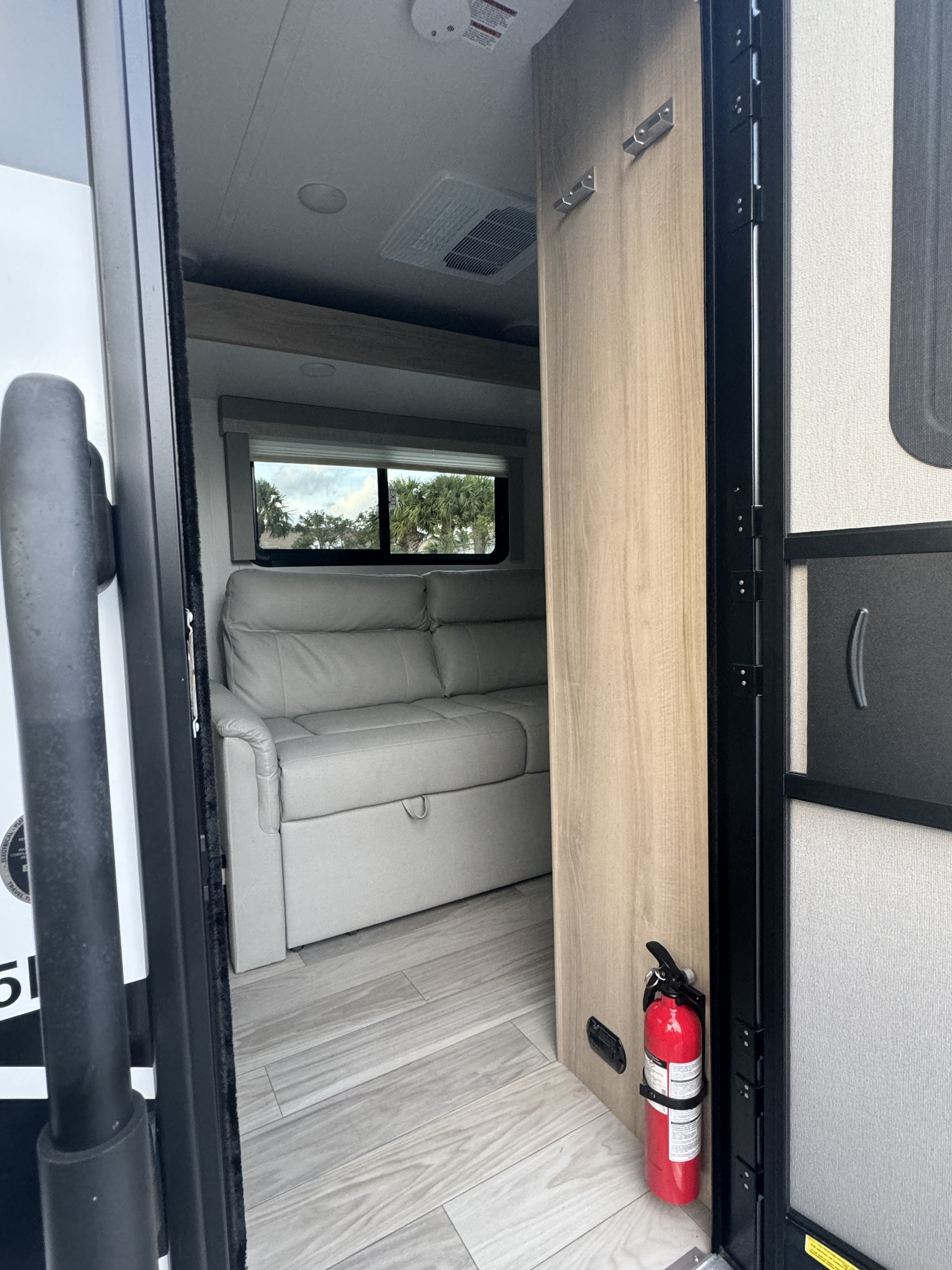 Step into this RV rental's inviting interior: light flooring, comfy sofa, window, and fire extinguisher by the door.. Minnie Micro Minnie 2024