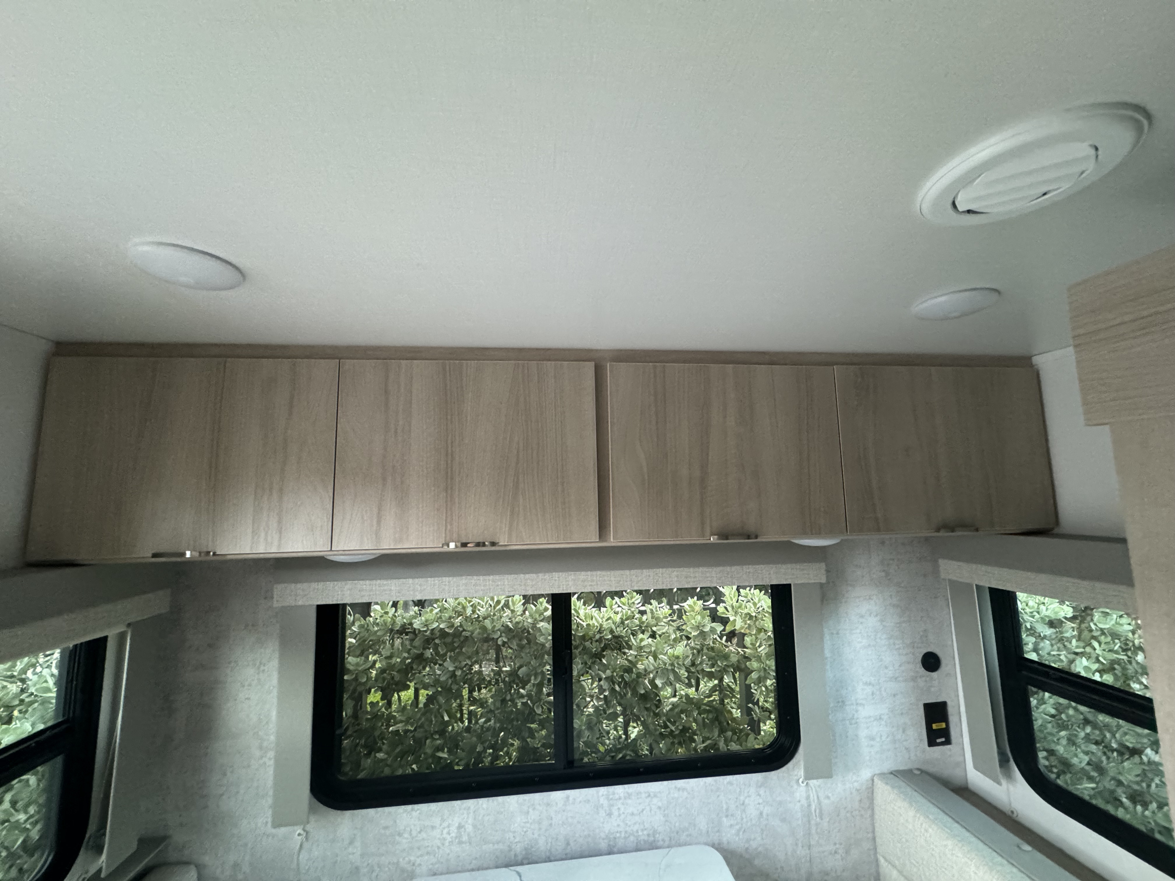 Bright RV rental interior features overhead light wood cabinets, ceiling lights/vent, and a window with green view.. Minnie Micro Minnie 2024