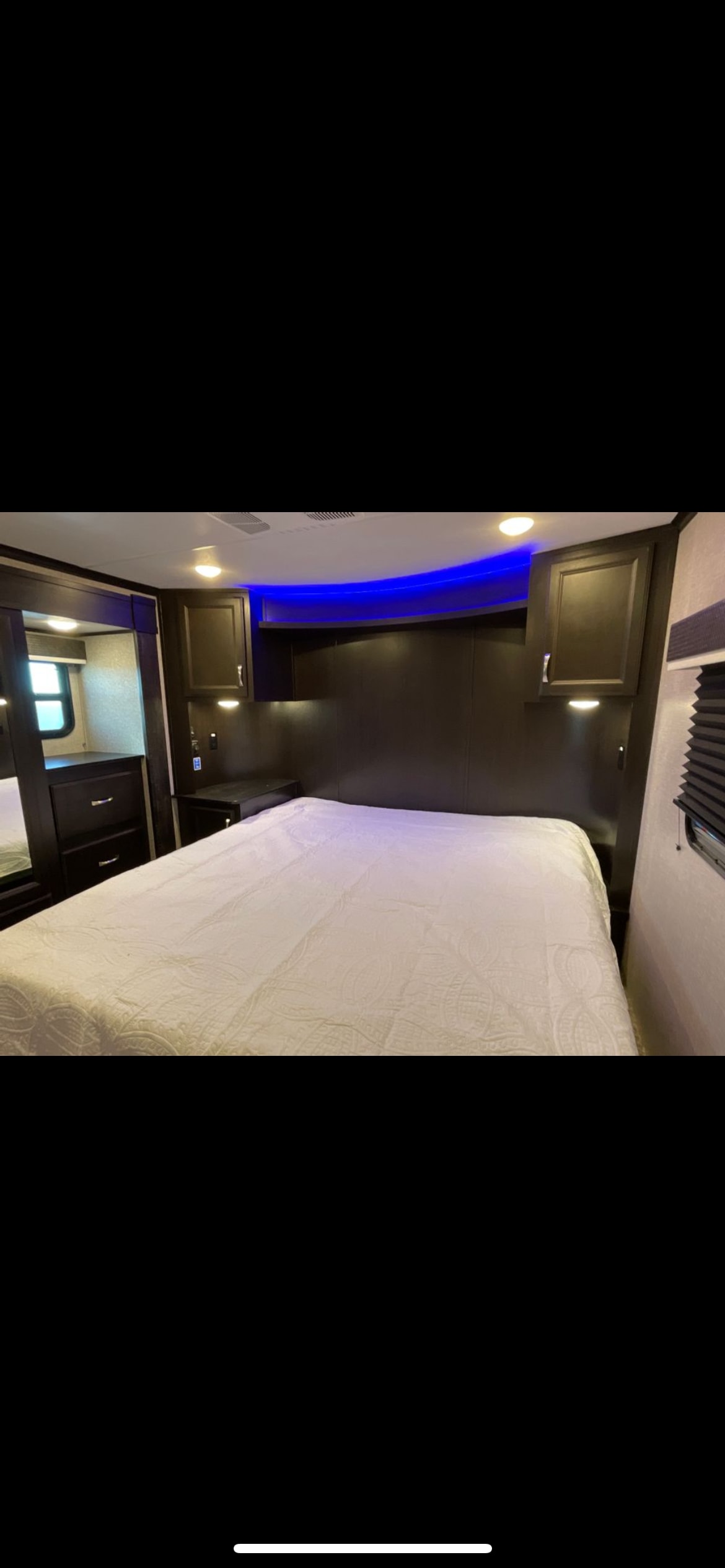 Spacious RV rental bedroom with white bedding, dark wood storage, and modern blue accent lighting for a comfortable stay.. Jayco Seismic 2023