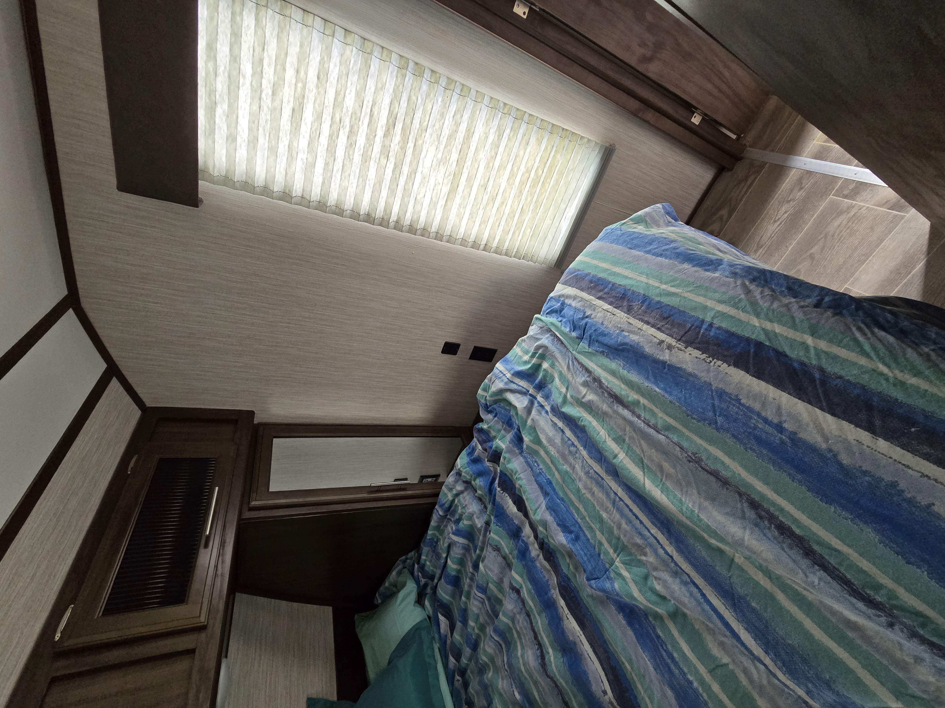 Cozy RV rental bedroom with striped bedding, overhead window, and storage, perfect for a comfortable trip.. Forest River Cherokee Alpha Wolf 2019
