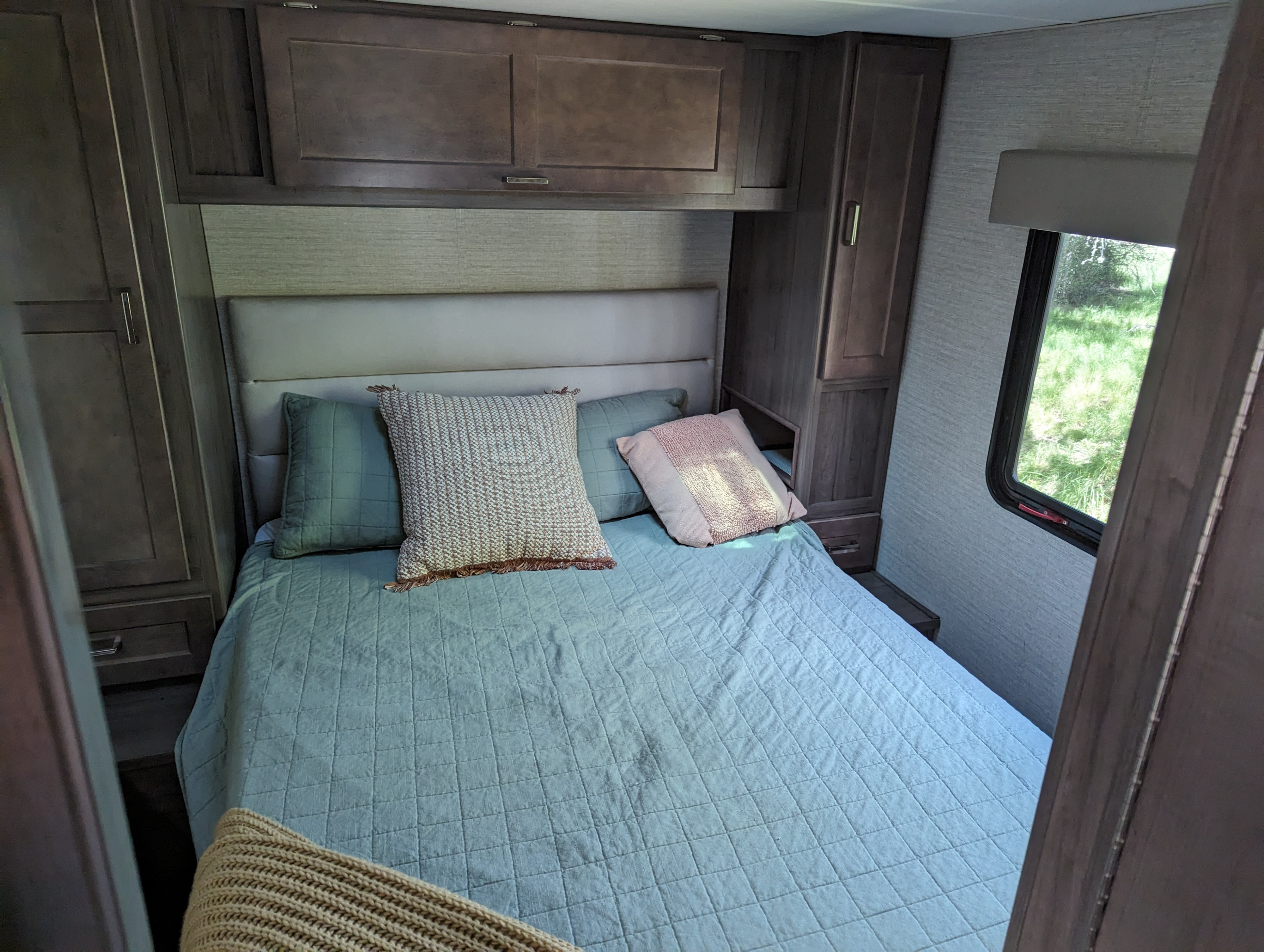 Cozy RV rental bedroom with a comfy bed, quilted teal bedding, decorative pillows, and built-in wood cabinets.. Winnebago Minnie Winnie 2020