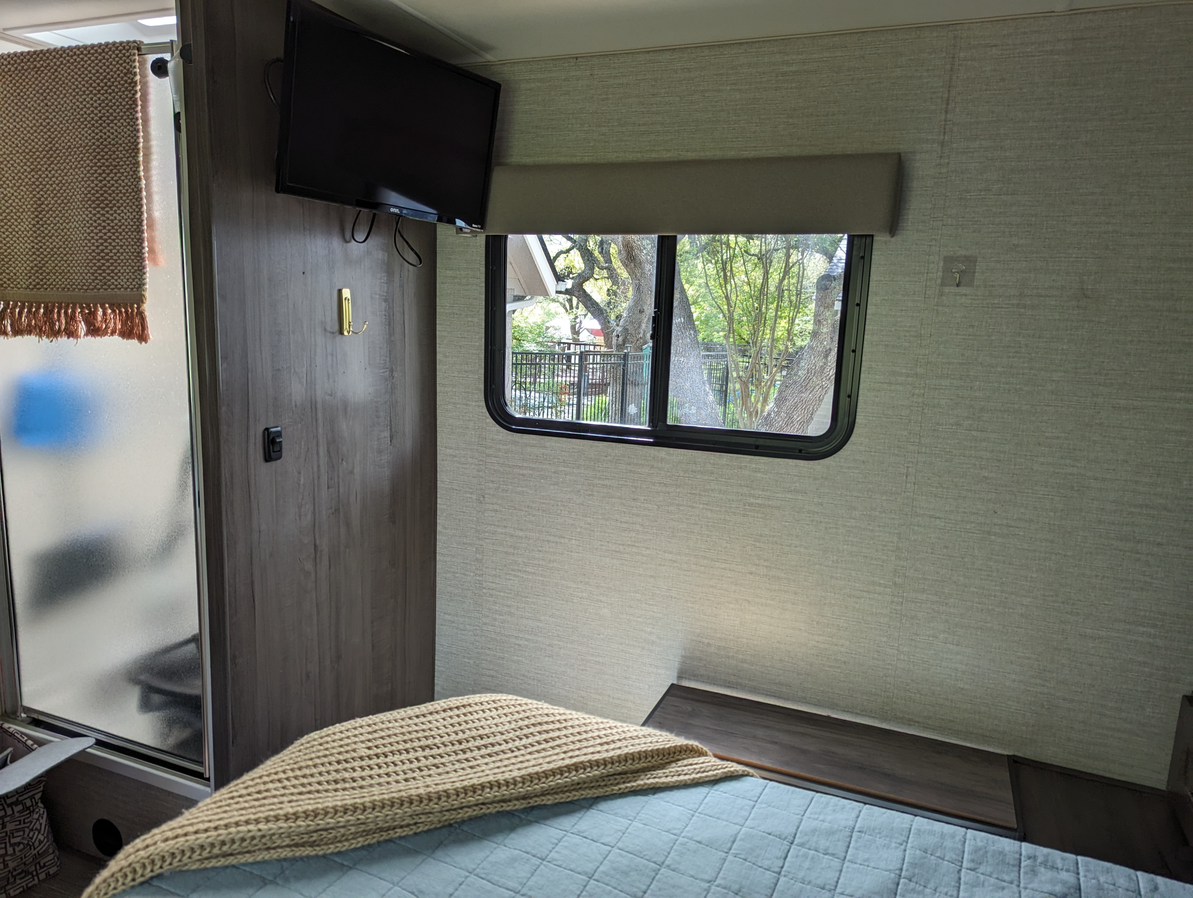 Cozy RV rental bedroom: light blue bed, TV, frosted shower, and window with outdoor tree view.. Winnebago Minnie Winnie 2020