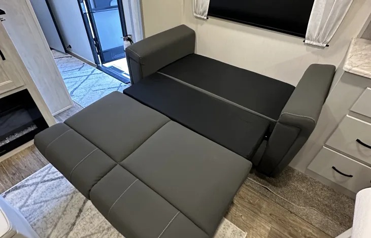 Gray sofa bed partially extended inside an RV rental. Modern interior with wood-look floor and mounted TV.. Forest River Vibe 2022