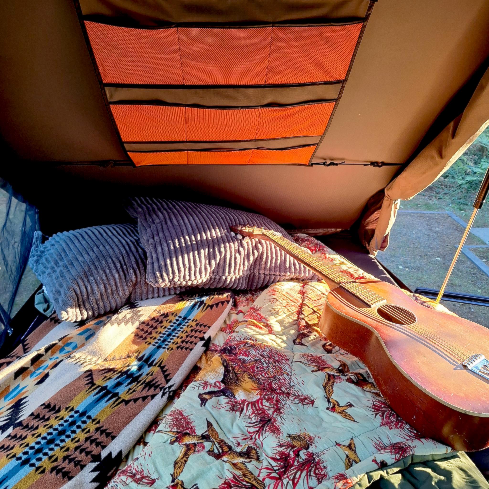 Cozy rooftop tent setup in an RV rental, featuring comfy pillows, blankets, and a guitar for relaxing.. Toyota FJ Cruiser 2009