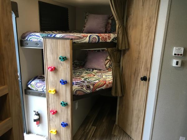 RV rental with fun bunk beds, featuring a built-in climbing wall for kids. Cozy sleeping space with colorful bedding and privacy curtains.. Coachmen Freedom Express Ultra Lite 2019