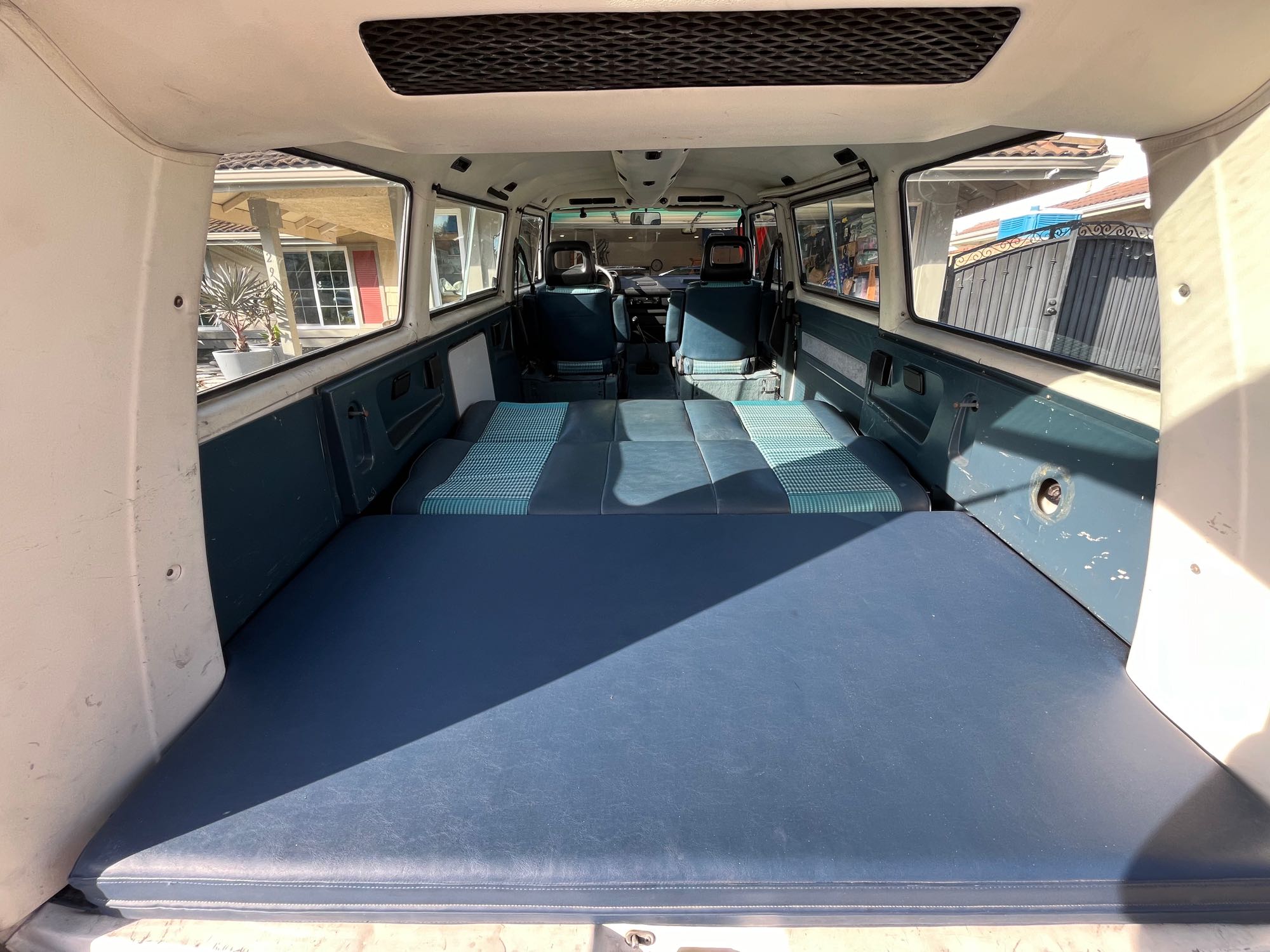An RV rental van's interior, viewed from the rear. Blue seats are folded flat, forming a bed; front cabin and windows are visible.. Volkswagen Vanagon 1987