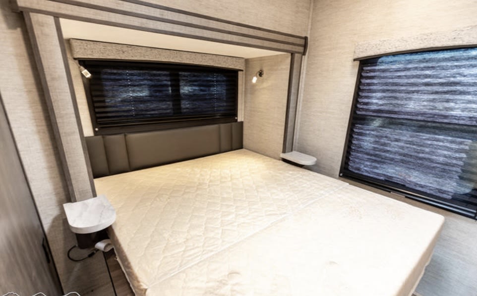 RV rental bedroom: A comfortable, neutral-toned space featuring a bed, window blinds, and compact nightstands.. Entegra Coach Odyssey 2022